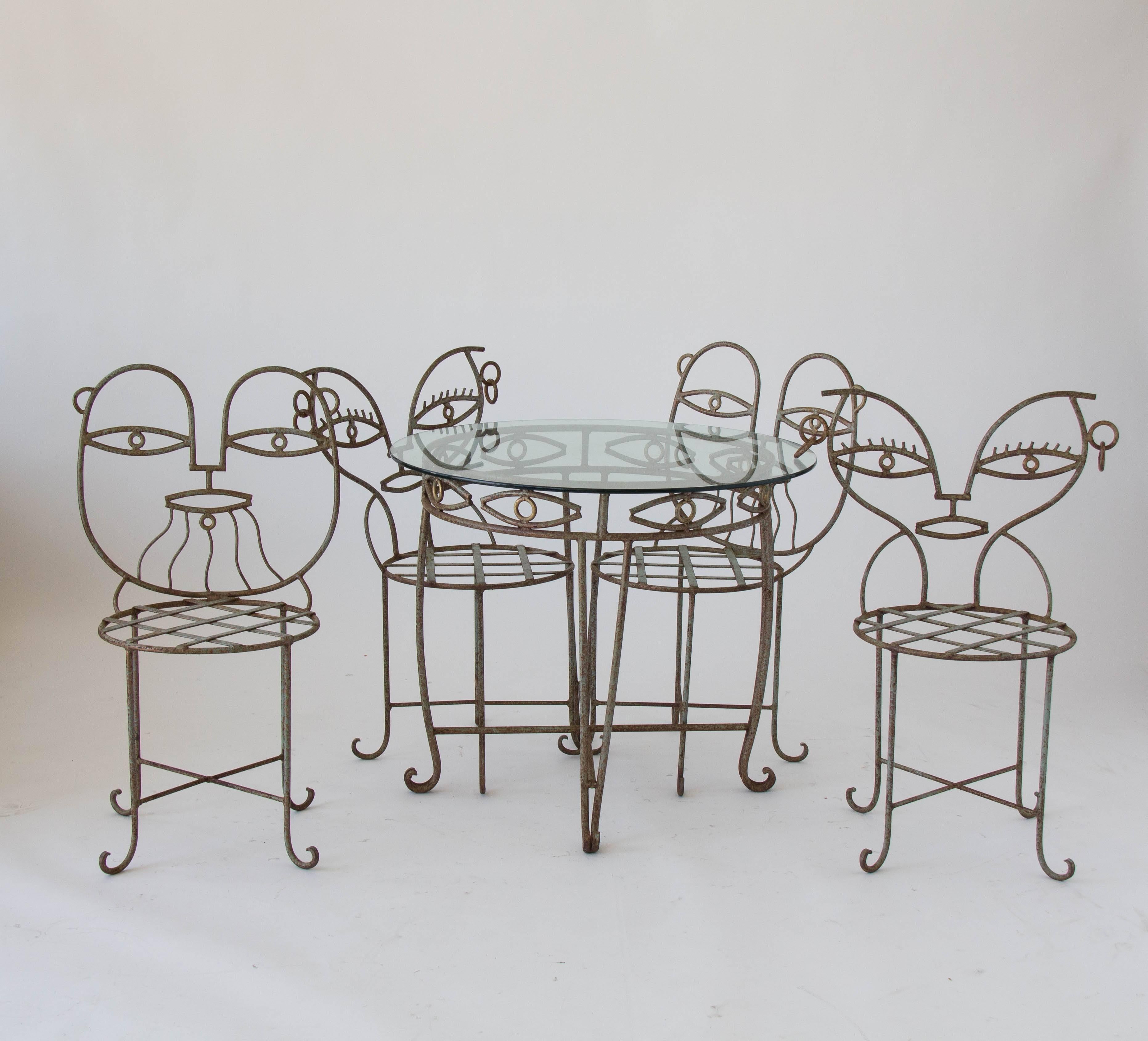 A wrought iron patio set in a cubist, Picasso-esque style. The set is composed of four chairs and a bistro-sized round table. Two of the chairs have a backrest that resembles masculine features with a stylized beard; the other two have feminine