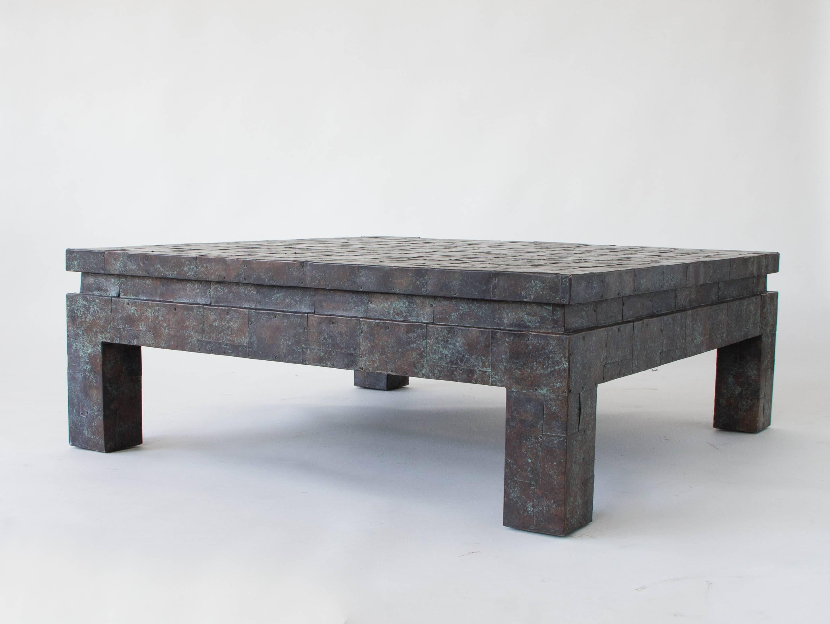 A monumental coffee table from North Carolina-based furniture company Maitland-Smith. The table has a wooden frame with block legs and a square body. The surface is covered with meticulously laid sheets of oxidized copper for a brutalist patchwork