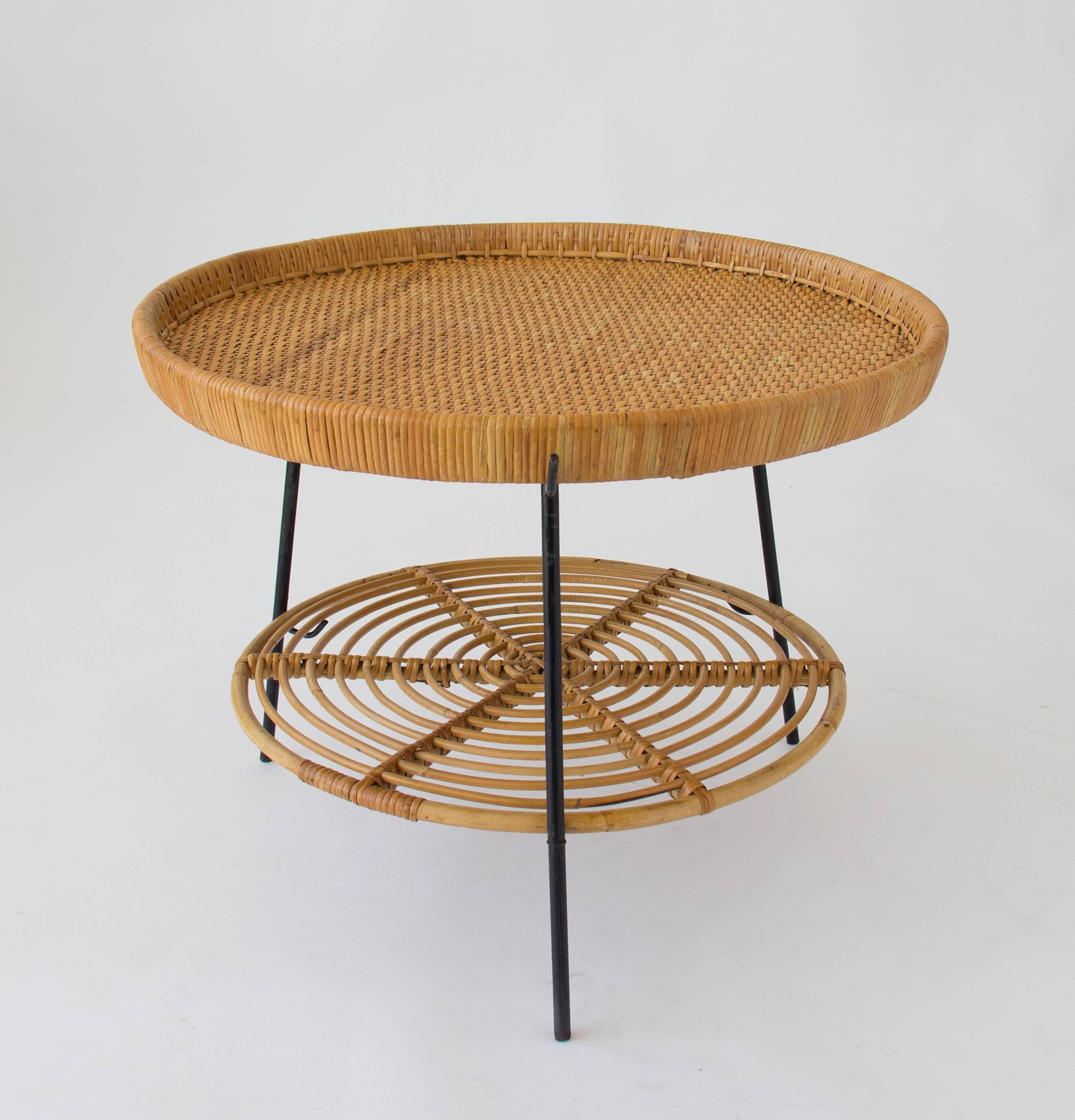 Deceptively simple tripod side table with wrought iron legs and two tiers imported by Raymor. The rattan tabletop and shelf lift out of the frame to double as trays. The lower tier has a loose, basket weave while the upper one has a tighter weave
