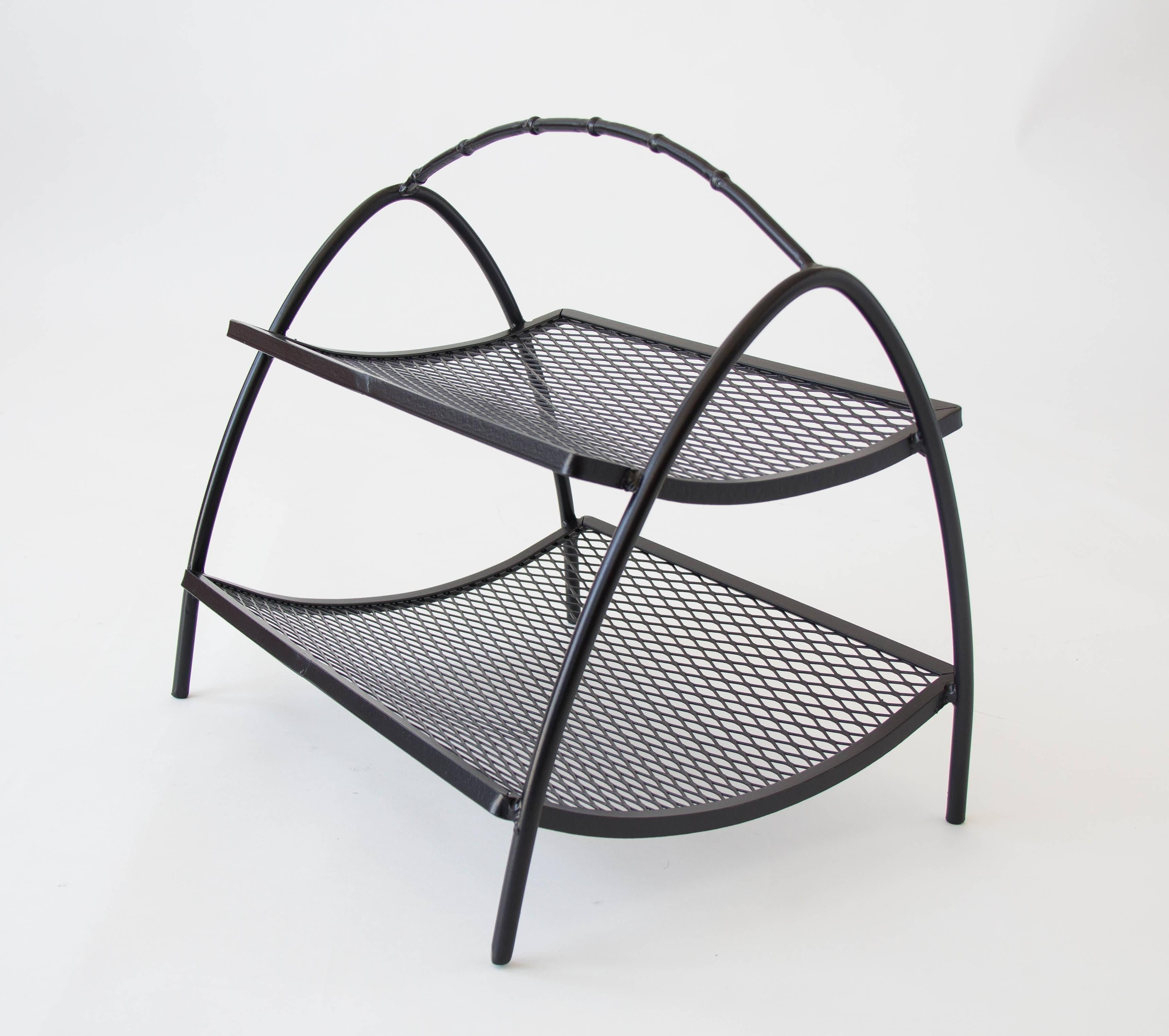 A simple wire magazine rack with two shelves of wire mesh. The shelves fit into a frame of two arched wires, joined by a central handle of faux-bamboo. 

Condition: Excellent restored condition; professionally powder-coated. 

Dimensions: 18
