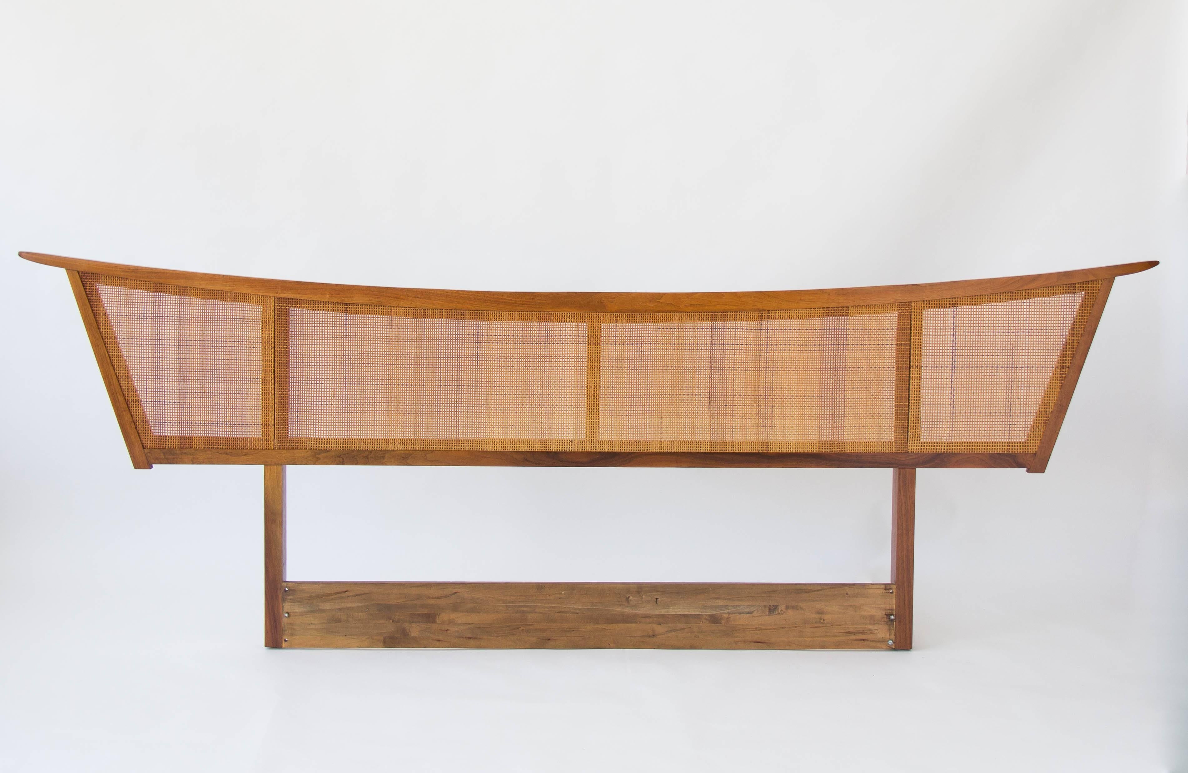 A walnut and cane headboard by George Nakashima for Widdicombe Furniture. From the "Origins" line, this Shaker-inspired piece has an exaggerated frame with a bowed top edge. The original woven cane panel fills the frame and contrasts with