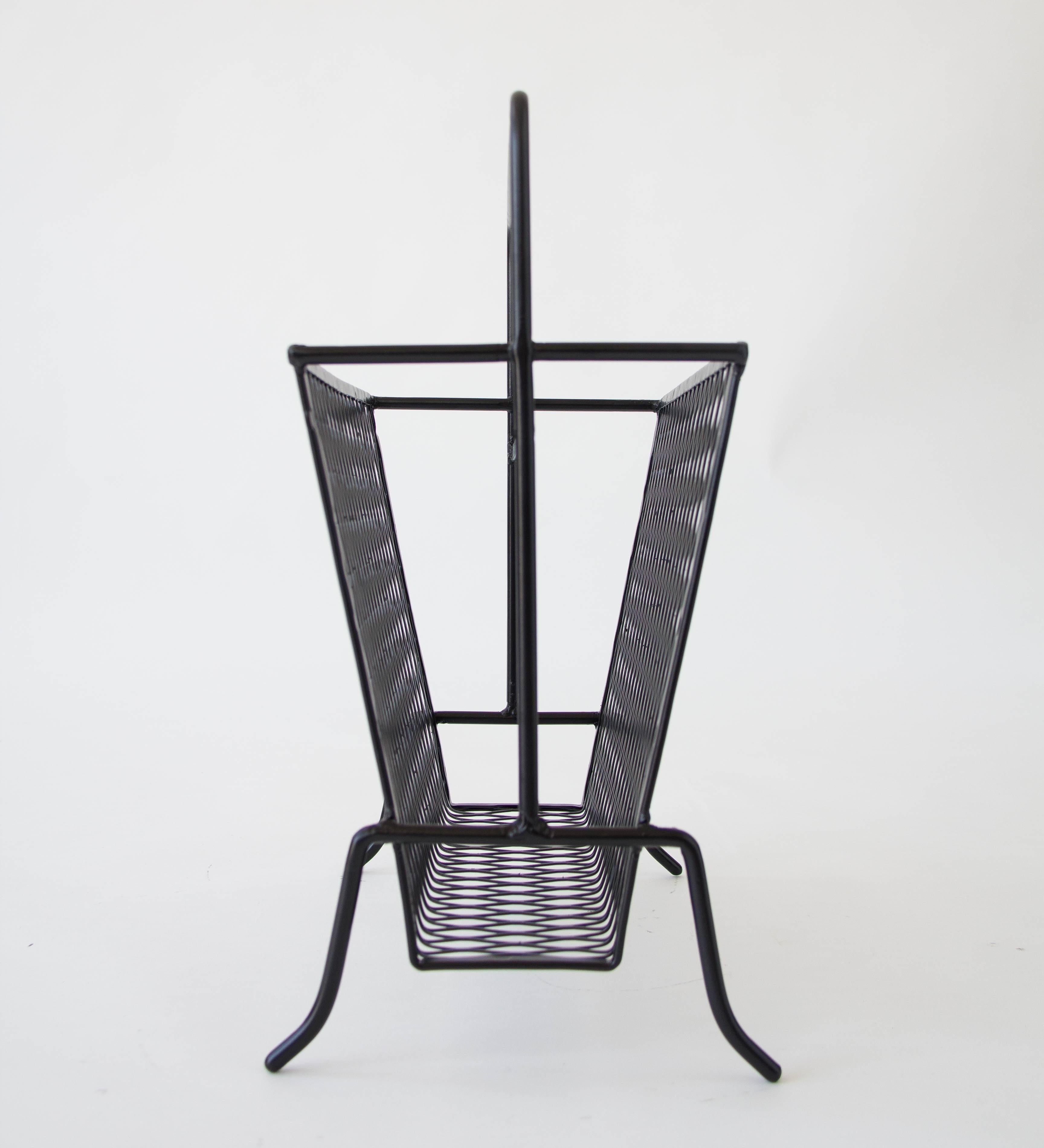 A Salterini-inspired wire magazine rack with wire mesh sides, a central handle, and four stylistically bent legs. The upright storage has slightly angled sides. 

Condition: Excellent restored condition; professionally powder-coated.