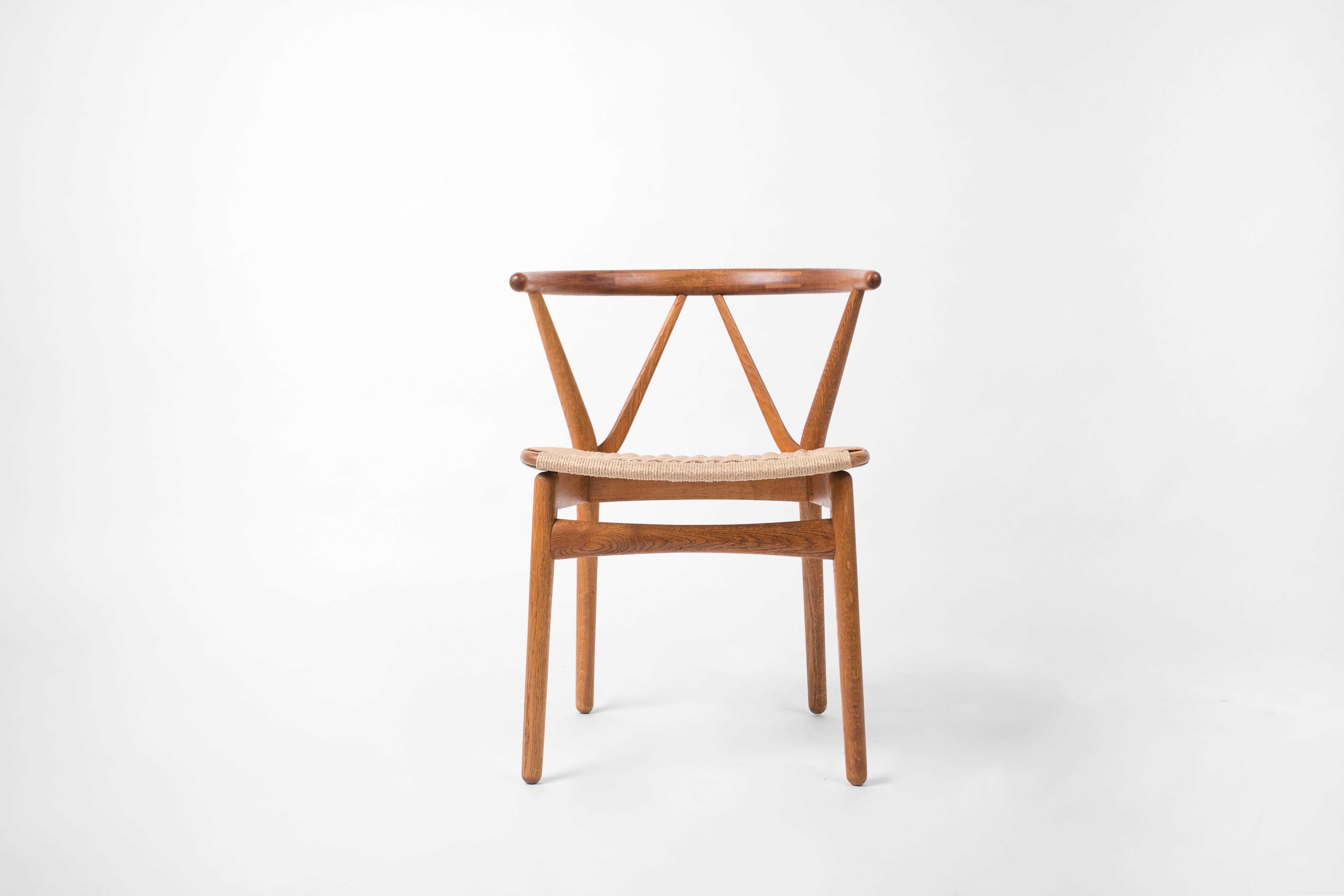 A set of six Danish modern dining chairs from Henning Kjaernulf, produced by Bruno Hansen. Constructed in teak, with woven fibre rush (also known as paper cord) seat, the curved backrest and angled supports of this design are reminiscent of Hans