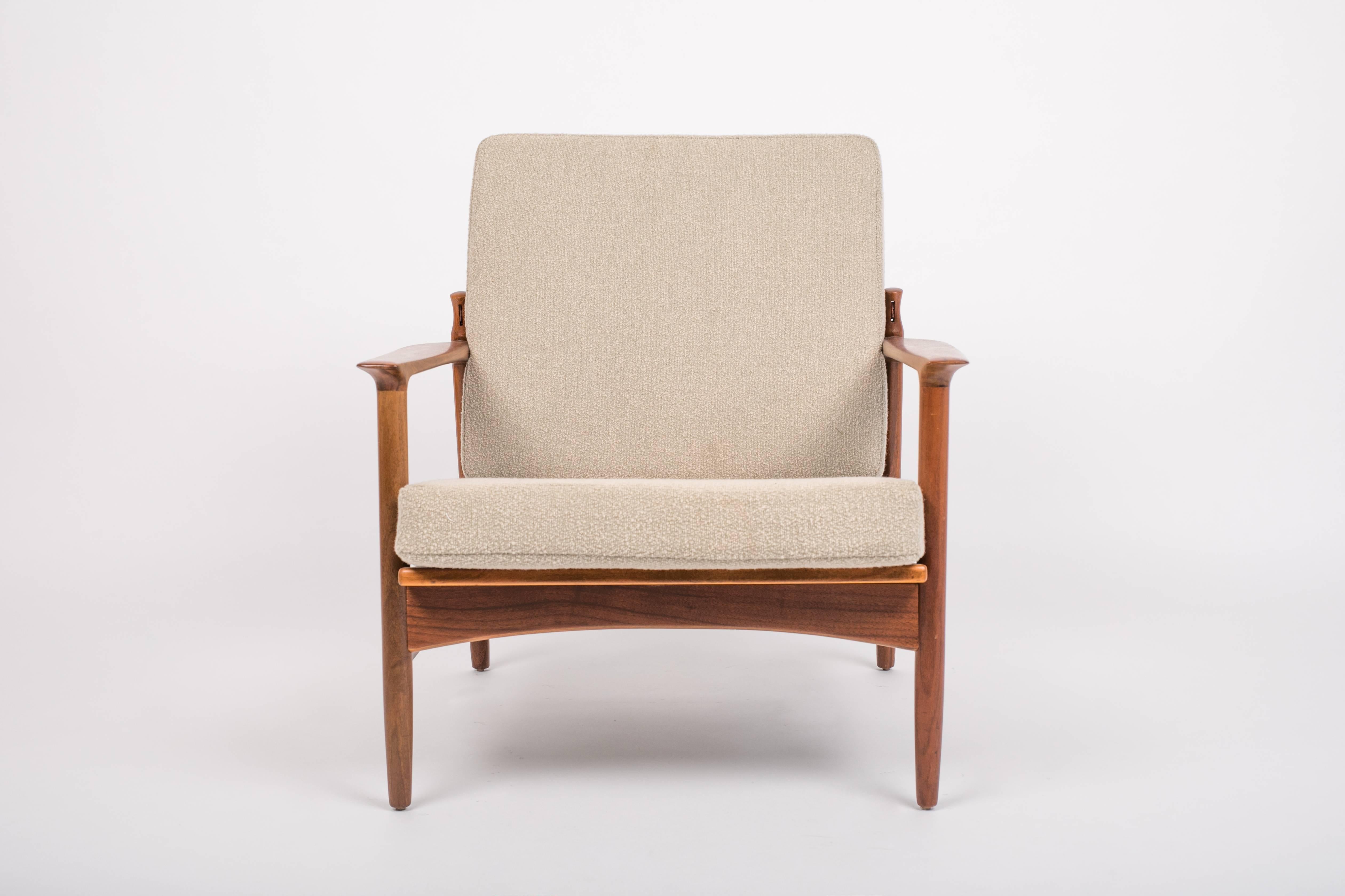 A unusual Ib Kofod Larsen design imported to the US by Selig has a frame of walnut-stained beech with creamy bouclé cushions. The chair has an adjustable angle of recline, with the backrest attached to the chair frame at leather straps with three