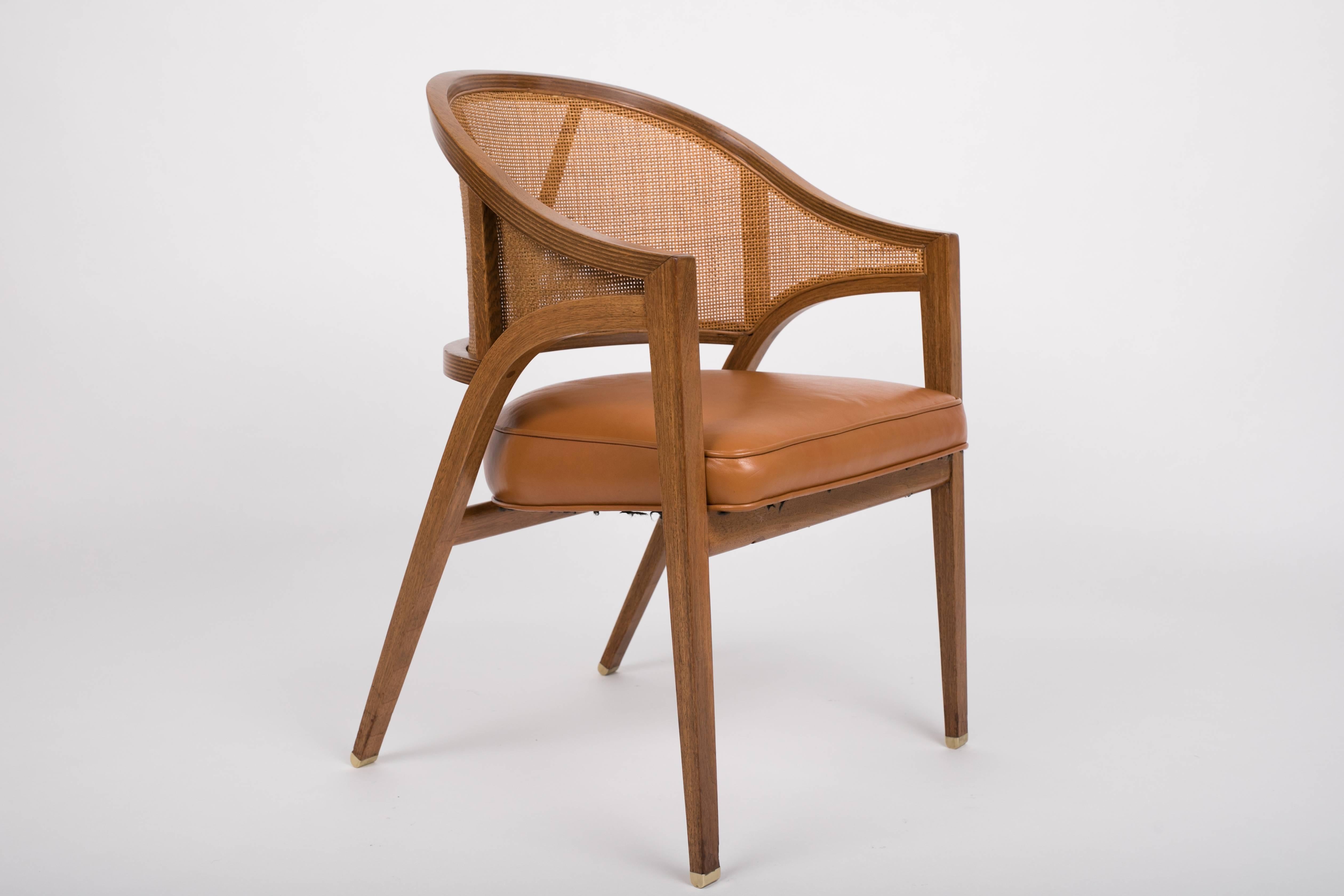 An elegant captain chair from designed by Edward Wormley and produced by Dunbar in the 1950s. It is a walnut armchair with a shell-like, curved backrest of basket-woven cane with an upholstered seat. The rails of the backrest are laminated walnut