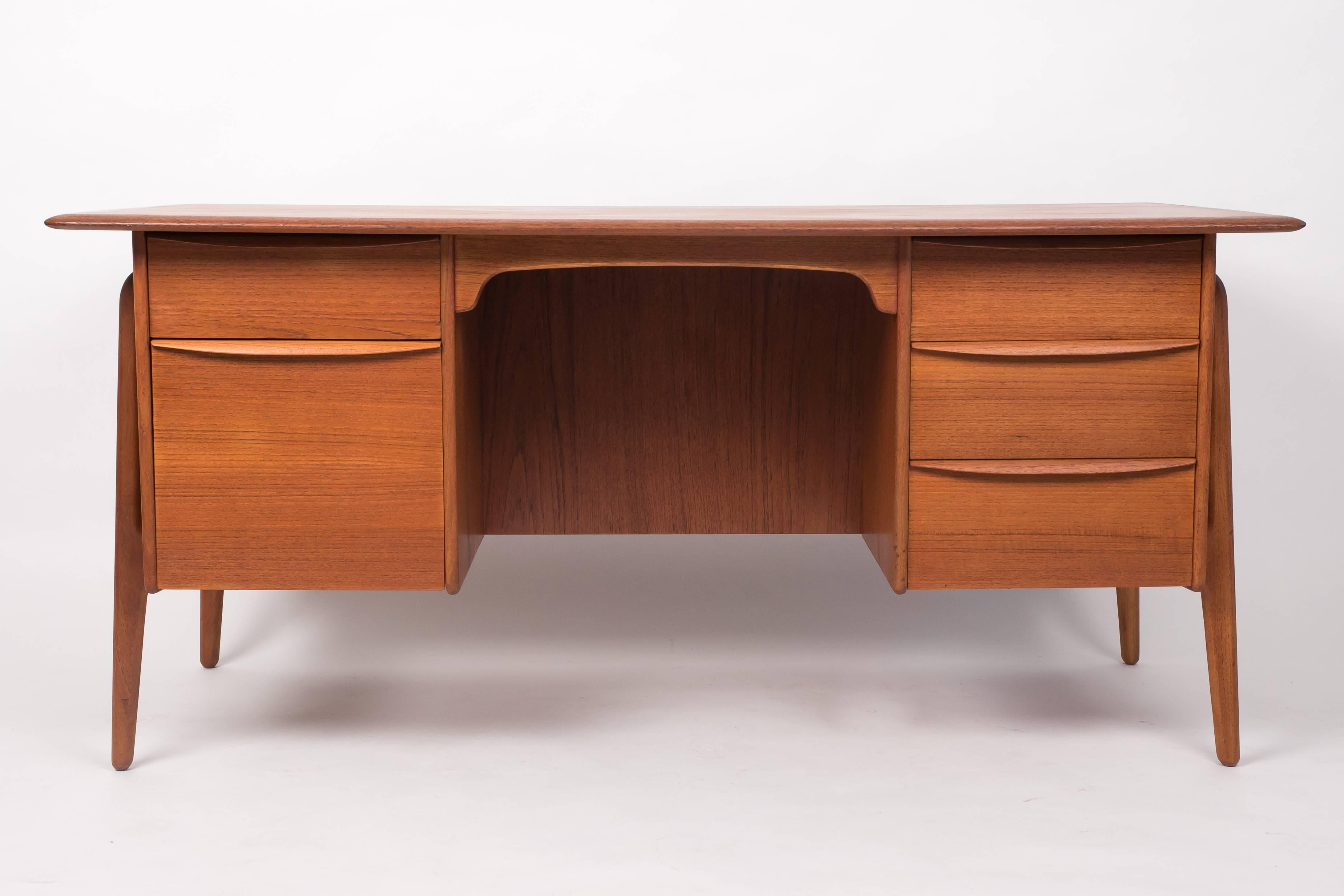Classic Danish teak executive desk with twin drawer stacks and a broad writing surface. This piece, designed by Svend Åage Madsen for Sigurd Hansen is distinguished by the bookcase that runs lengthwise along its back panel and the end-pieces of