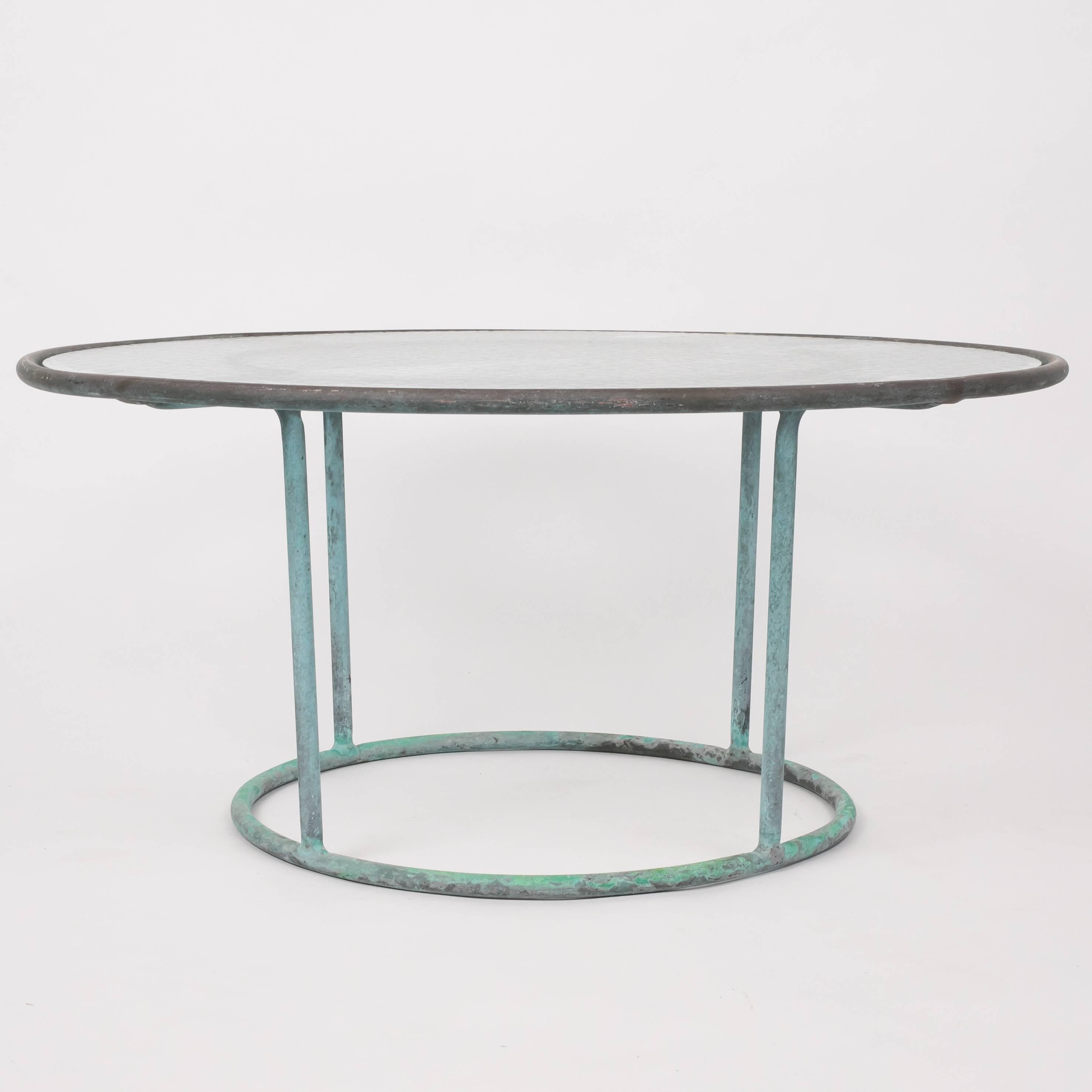 A patio coffee table in patinated bronze designed by Walter Lamb and produced by Brown Jordan. The monumental frame is described by two concentric rings of bronze with radial supports and a circular bronze base. The round tabletop is a single piece