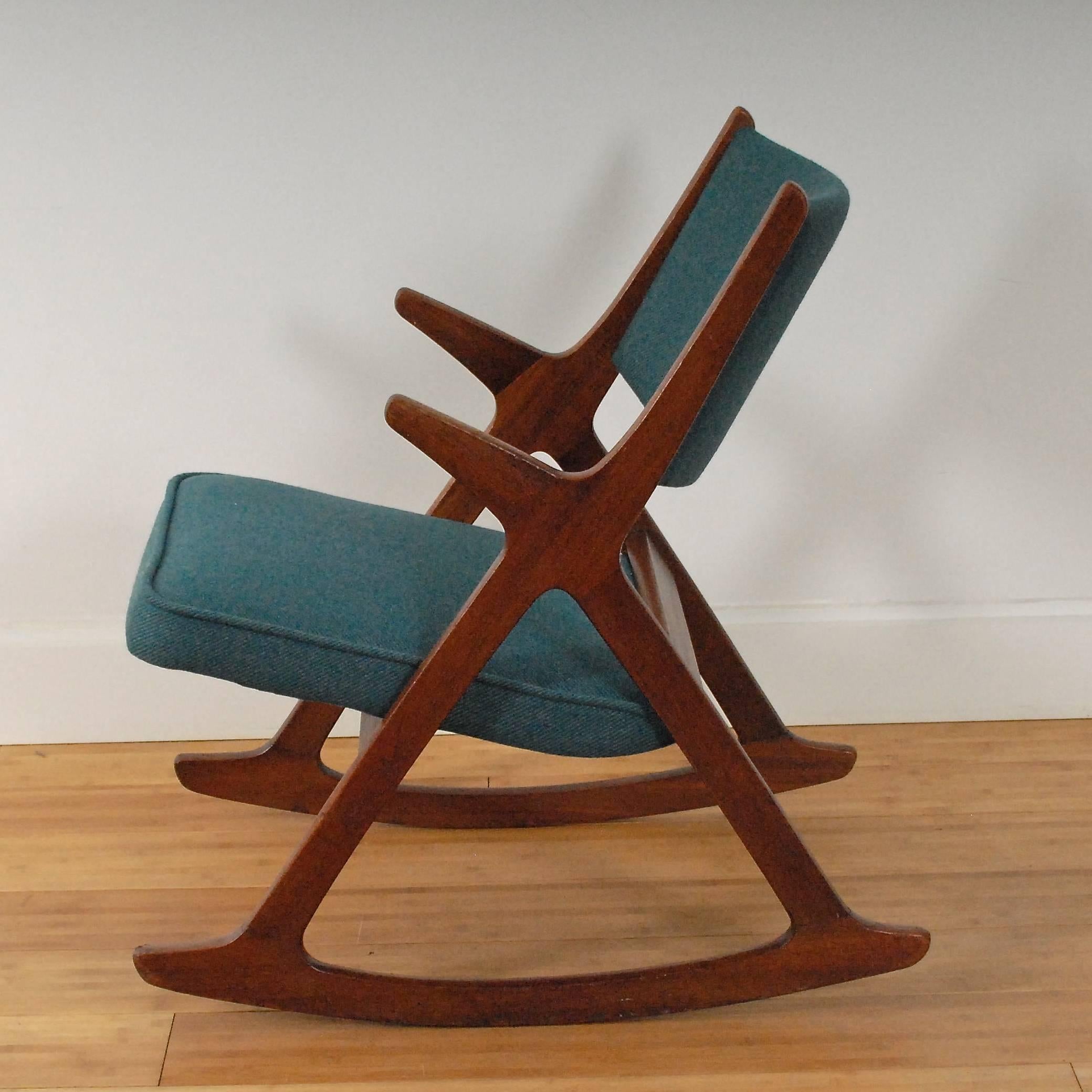 Norwegian rocking chair with cross base in massive teak. 

Reupholstered with fabric from Norwegian manufacturer Gudbransdalen Ullvarefabrikk GU. 

