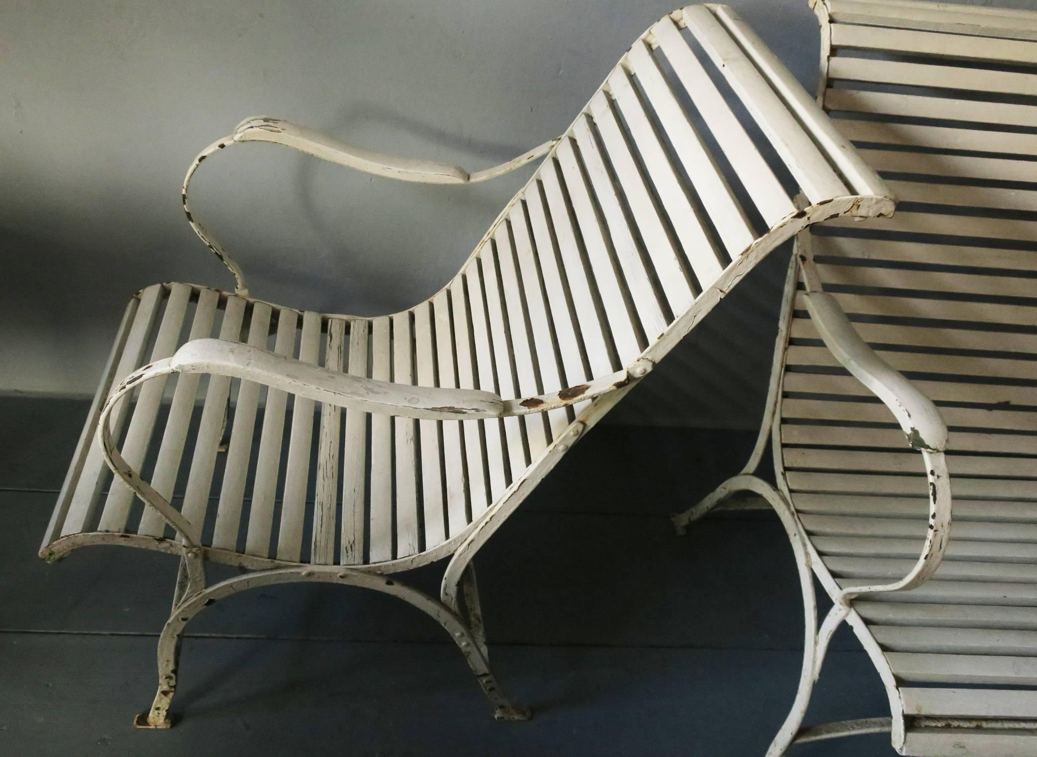 Pair of painted iron patio or garden lounge chairs, early 20th century.

The chairs have an iron frame with wood slats for the seat and back and wood armrests.