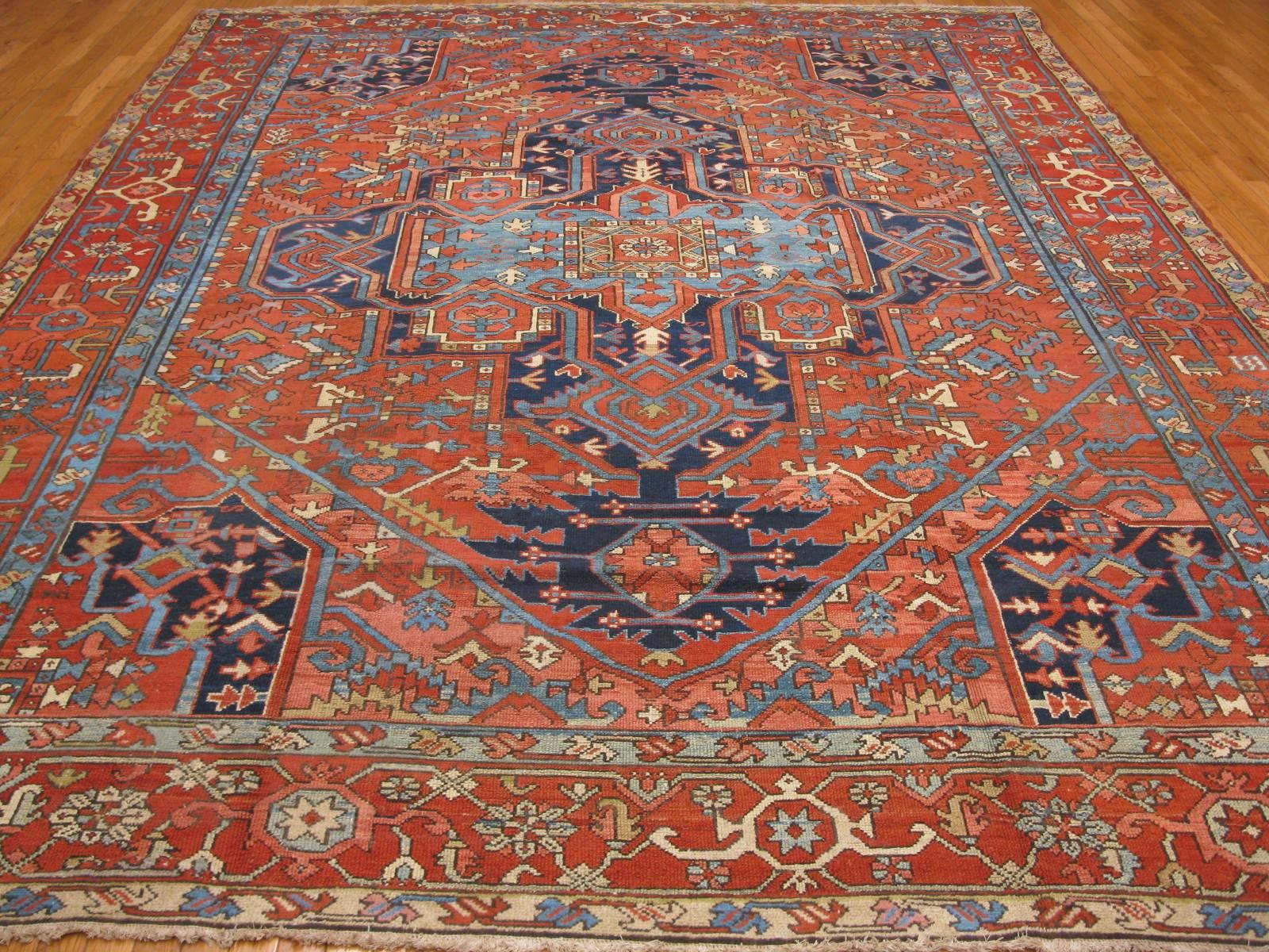 This is a room size traditional hand-knotted antique Persian Serapi rug in rich warm brick red color contrasted by navy blue medallion and corners. It is a perfect choice for almost any room in your home or office. The rug measures 9' 6'' x 12'