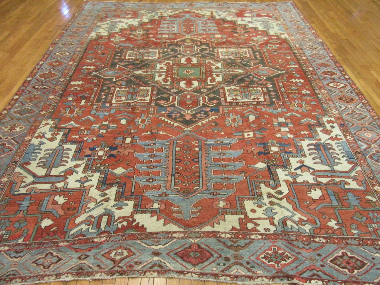 This is an antique hand-knotted rugs from the village of Heriz in northwest Iran. The rug has a traditional geometric central and corner medallion design. It is made with natural wool colored with natural dyes on a cotton foundation. It has a