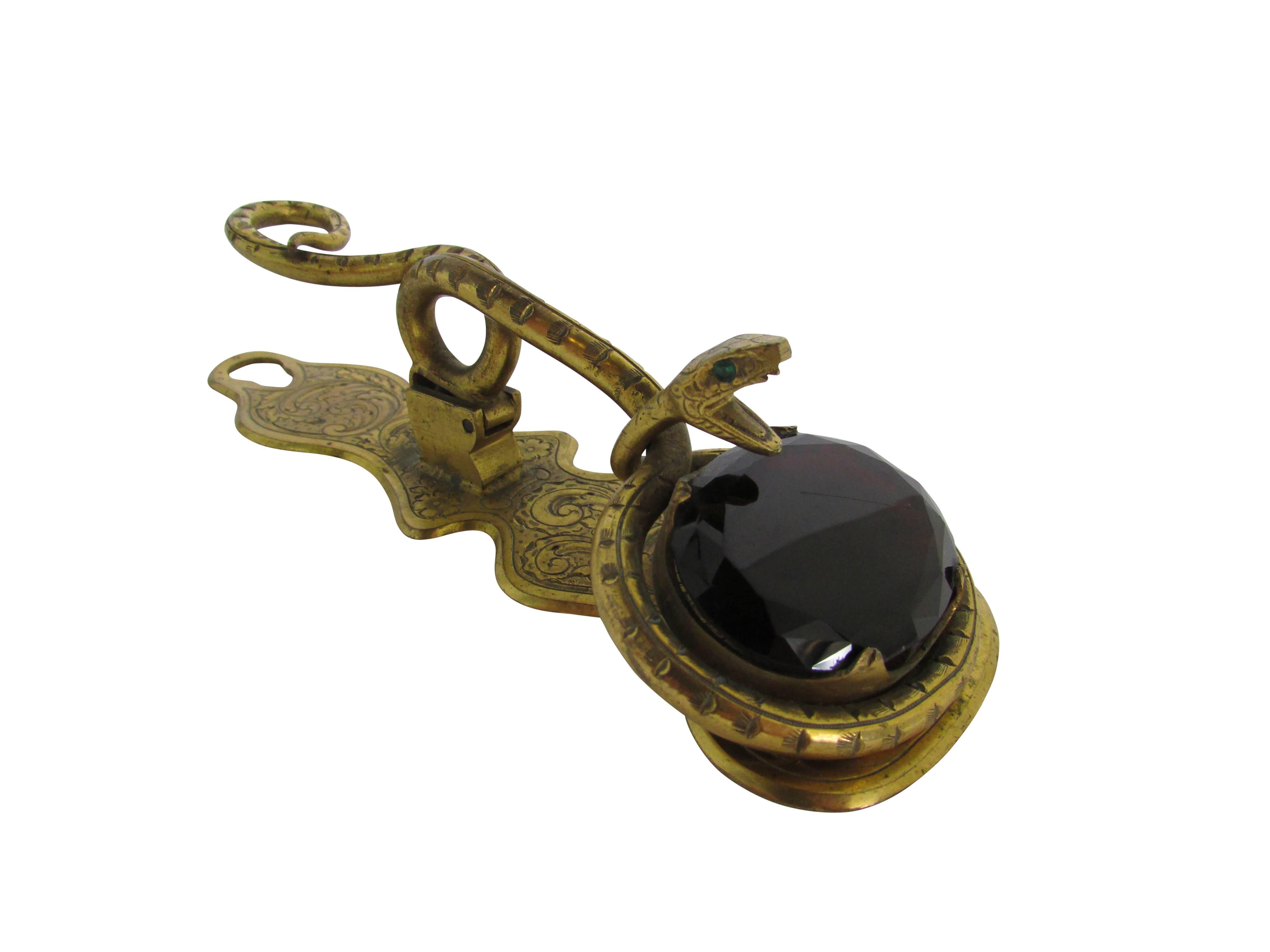 This is a brass Victorian era letter clip with a snake wrapped around a faceted garnet glass jewel. It can be mounted to the wall or sit desk top.