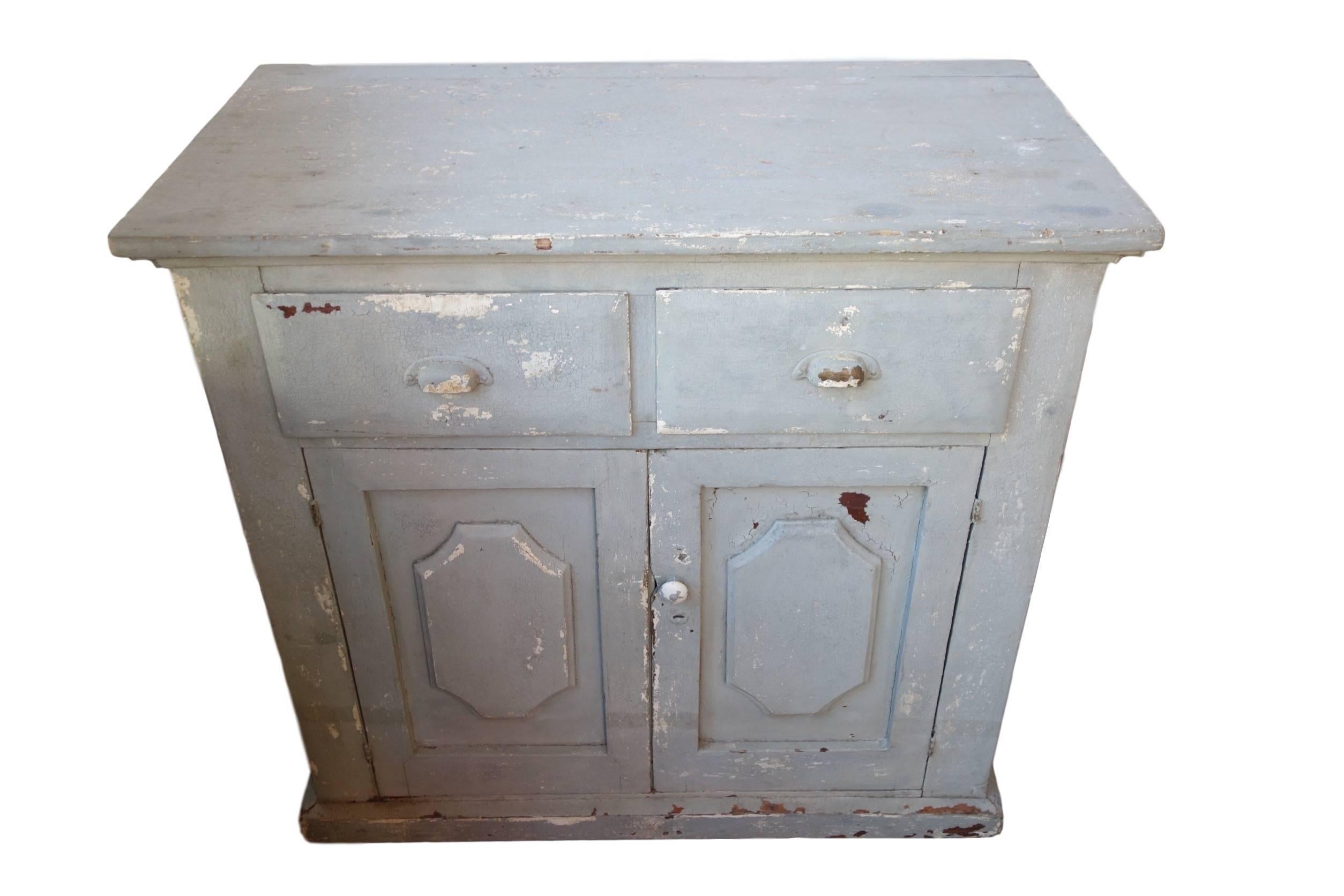 This is an early 20th century painted cabinet or dresser in its original blue/gray paint and all original hardware. This piece has plenty of storage with two drawers and a cabinet with an interior shelf. The bead board on the interior of the cabinet