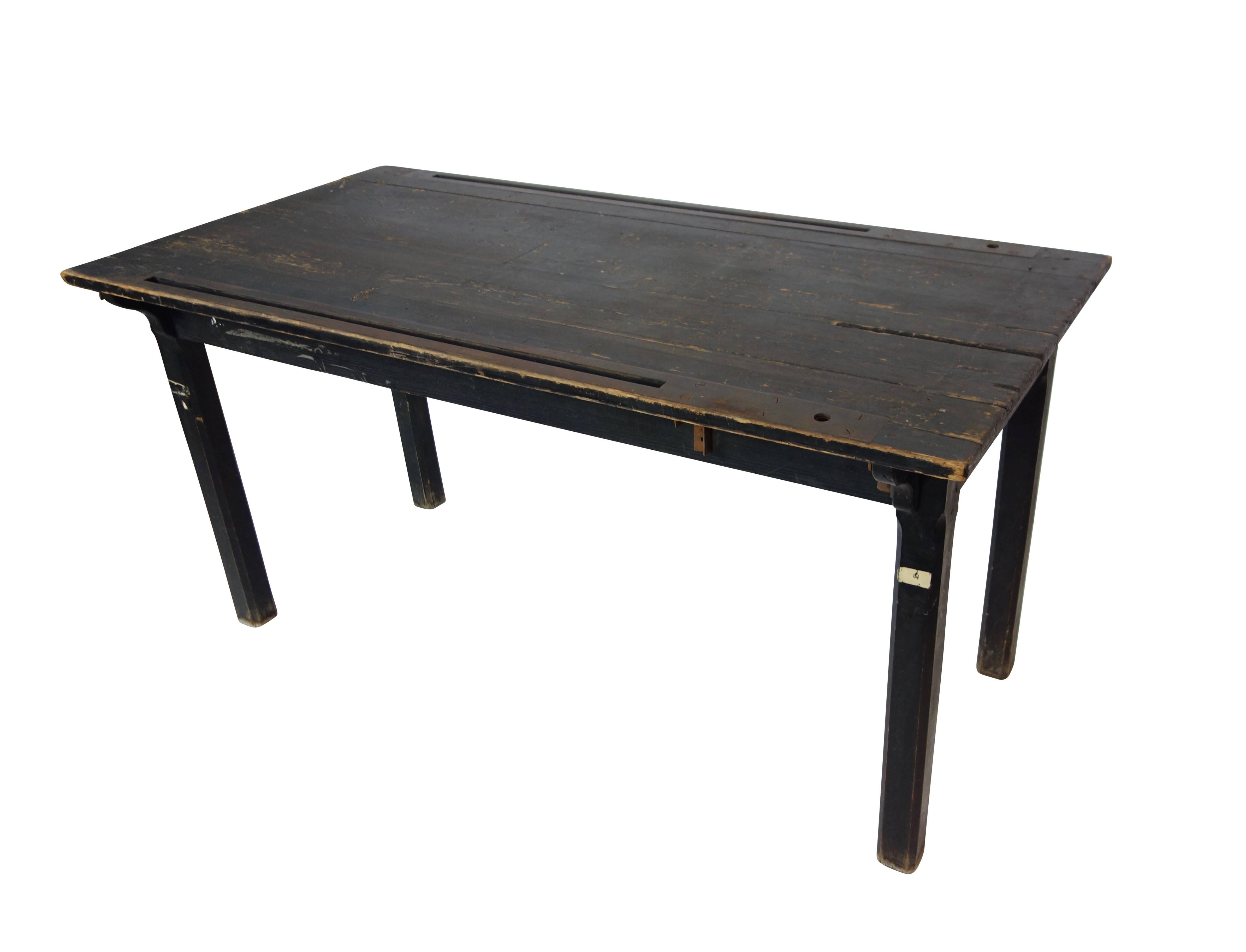 This is an early 20th century black painted Industrial wood dining table. The tabletop has two iron tracks that run lengthwise along the edge on either side of the table. Its original use is unknown, but this was once some kind of work table.