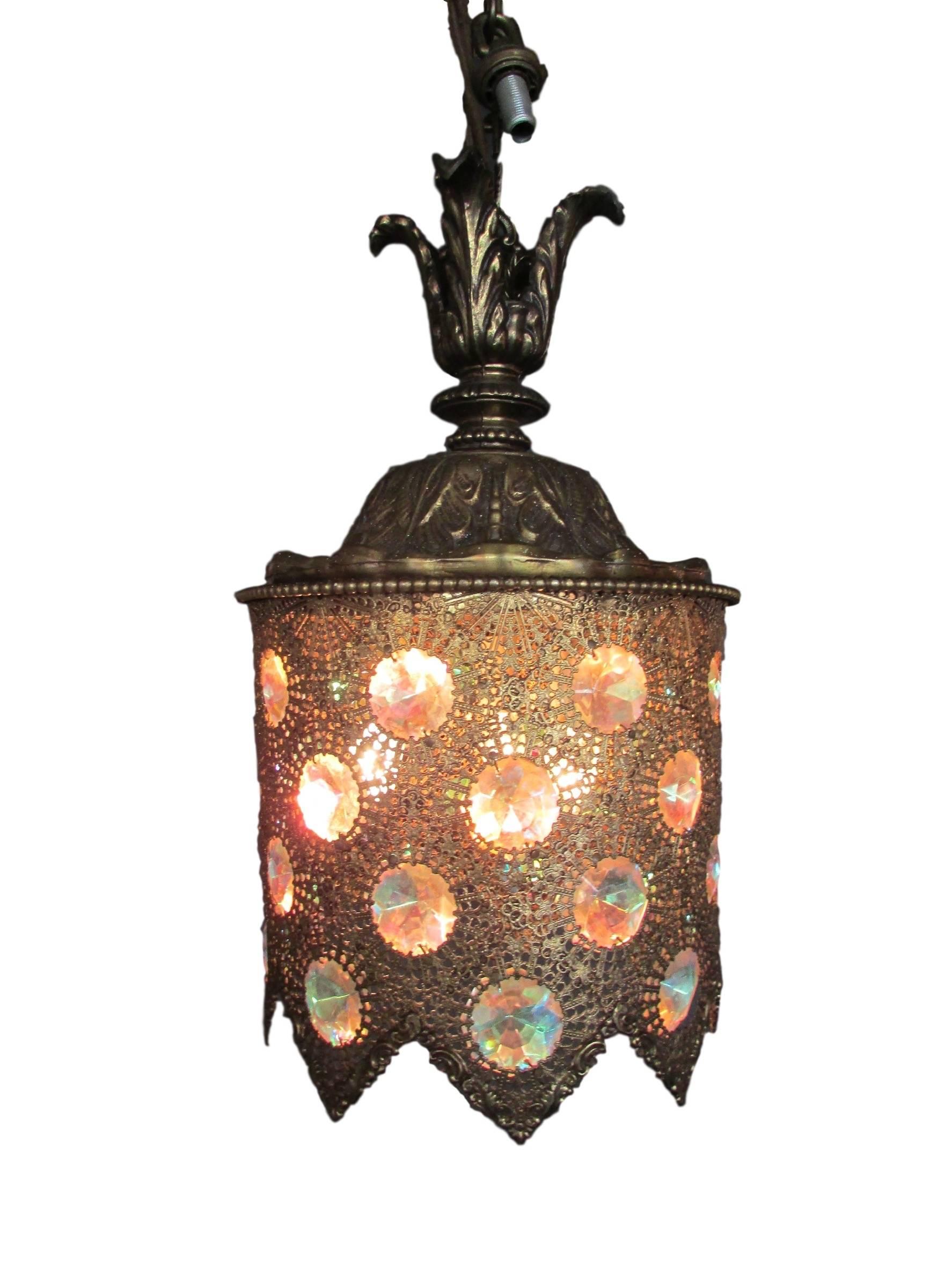 This is a brass filigree pendant light with beautiful cut iridescent jewels circa 1950.  When the light is turned off, the jewels appear blue.  When the light is turned on, the jewels appear pink. 