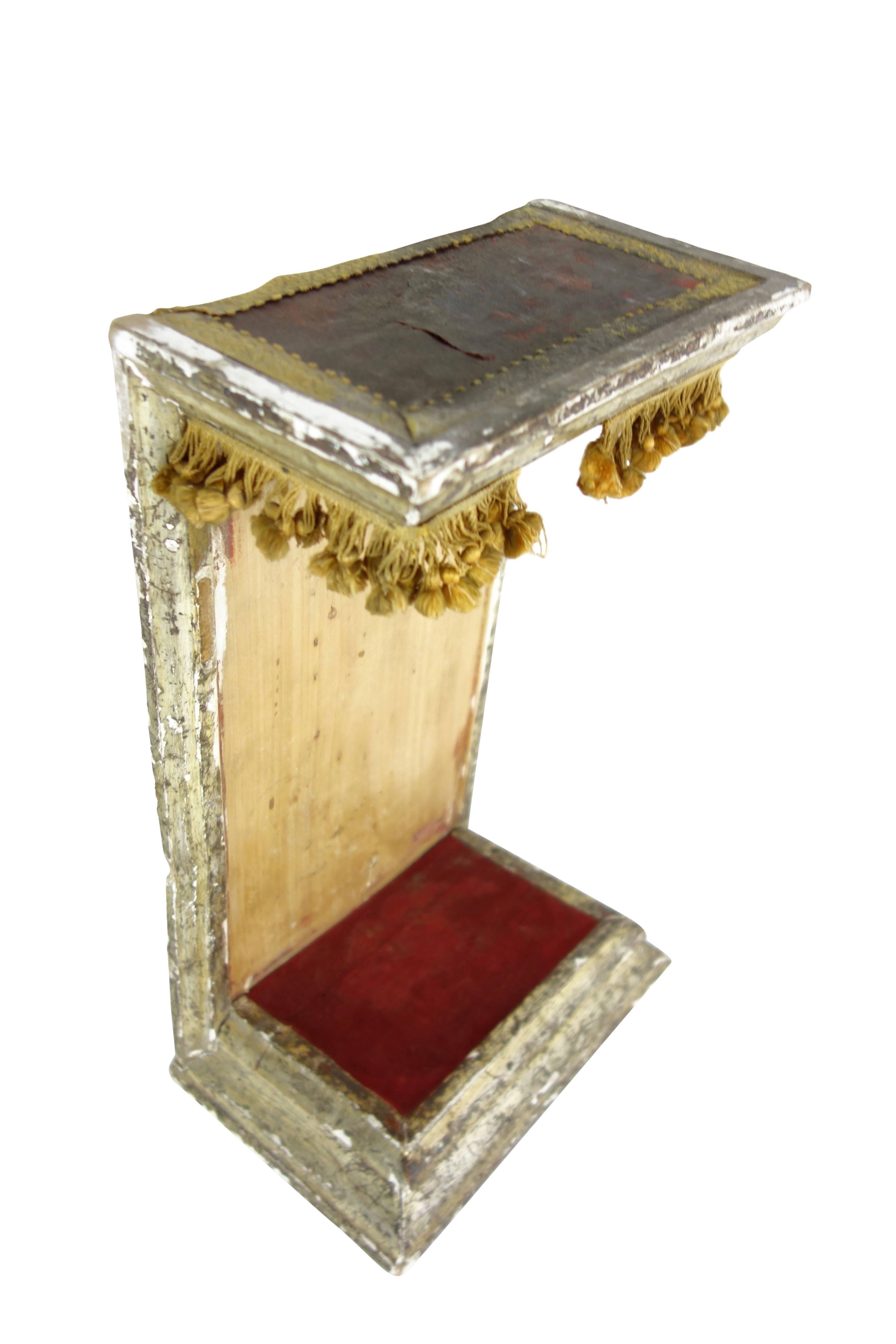 This is a turn of the century Italian saint display with red velvet raised platform and mustard colored pom pom trim. On the back there's a linen strap for a carrying handle.