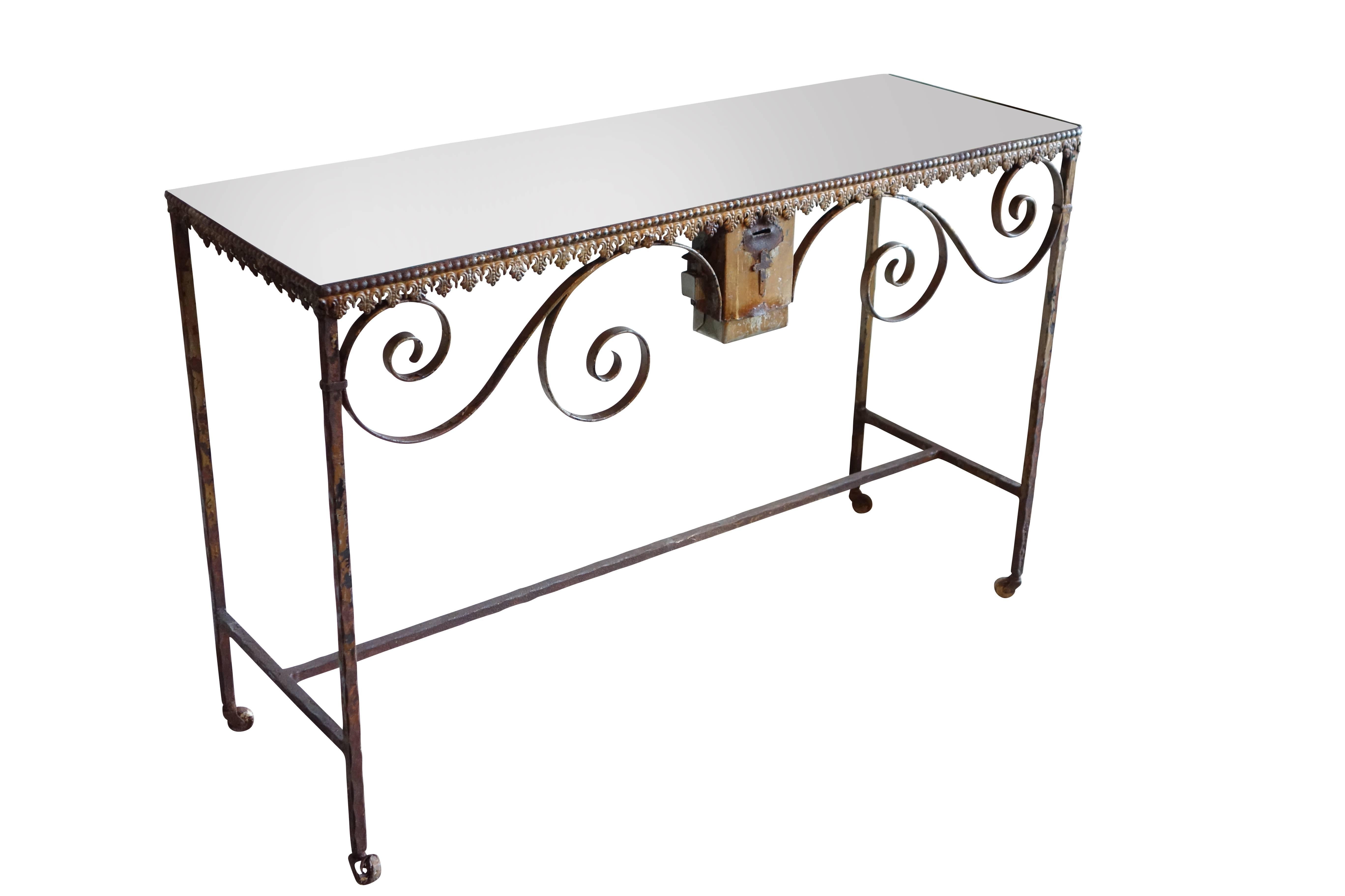 This is an early 20th century wrought iron offerings console with mirrored top on casters. Mounted to the front of the table is a lock box with cross detail where patrons of the church would make their deposits.