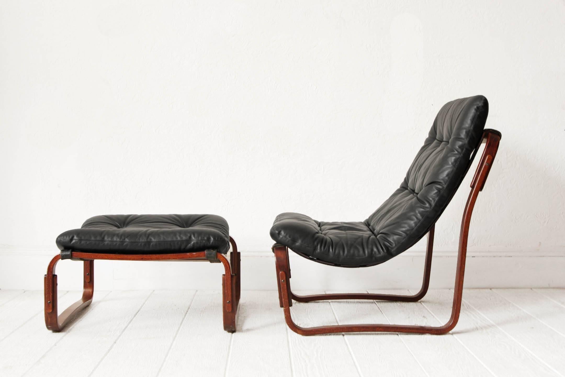 Lounge chair and ottoman by Ingmar Relling for Westnofa. Made in Norway / Scandinavian Modern. Black leather cushions on stained oak slat and leather 'sling' frame. The back of the cushions are an off-white canvas color. 
Measures:
Chair: 27.5
