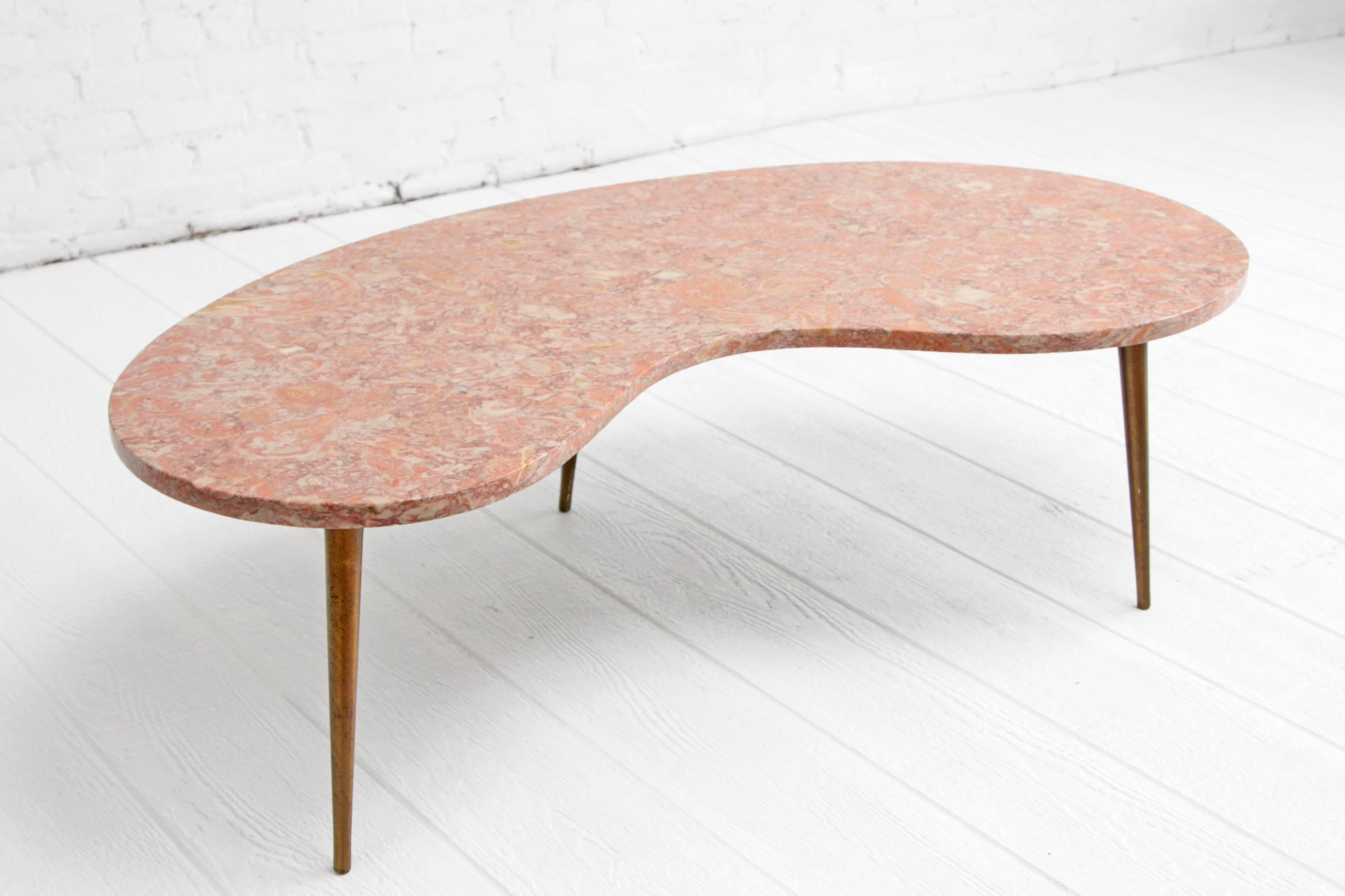Organic kidney shaped pink marble coffee table. The marble is suspended on three tapered brass legs that are attached to a smaller kidney shaped wood base.