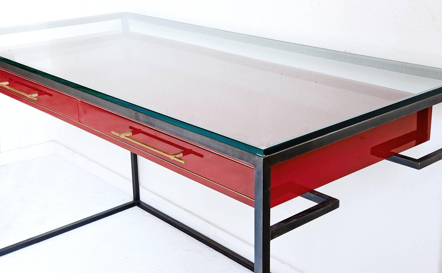This high-gloss red enamel desk is a sleek modern writing desk with brass inlay and drawer pulls set in a blackened steel frame.
