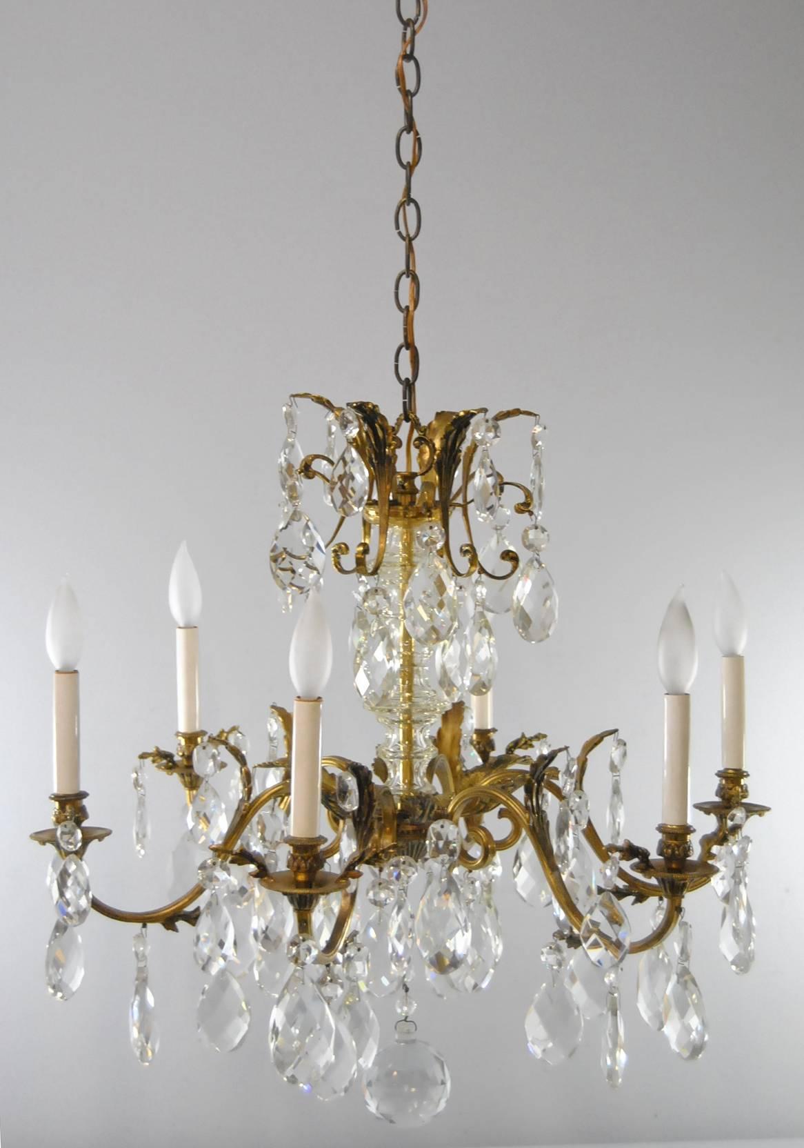 A beautiful six-arm French bronze chandelier with crystal prisms. The chandelier features six arms with each arm holding large 2 3/4 and 2 1/4 inch prisms. The central body has a formed glass tube which leads to a double tiered crown adorned with