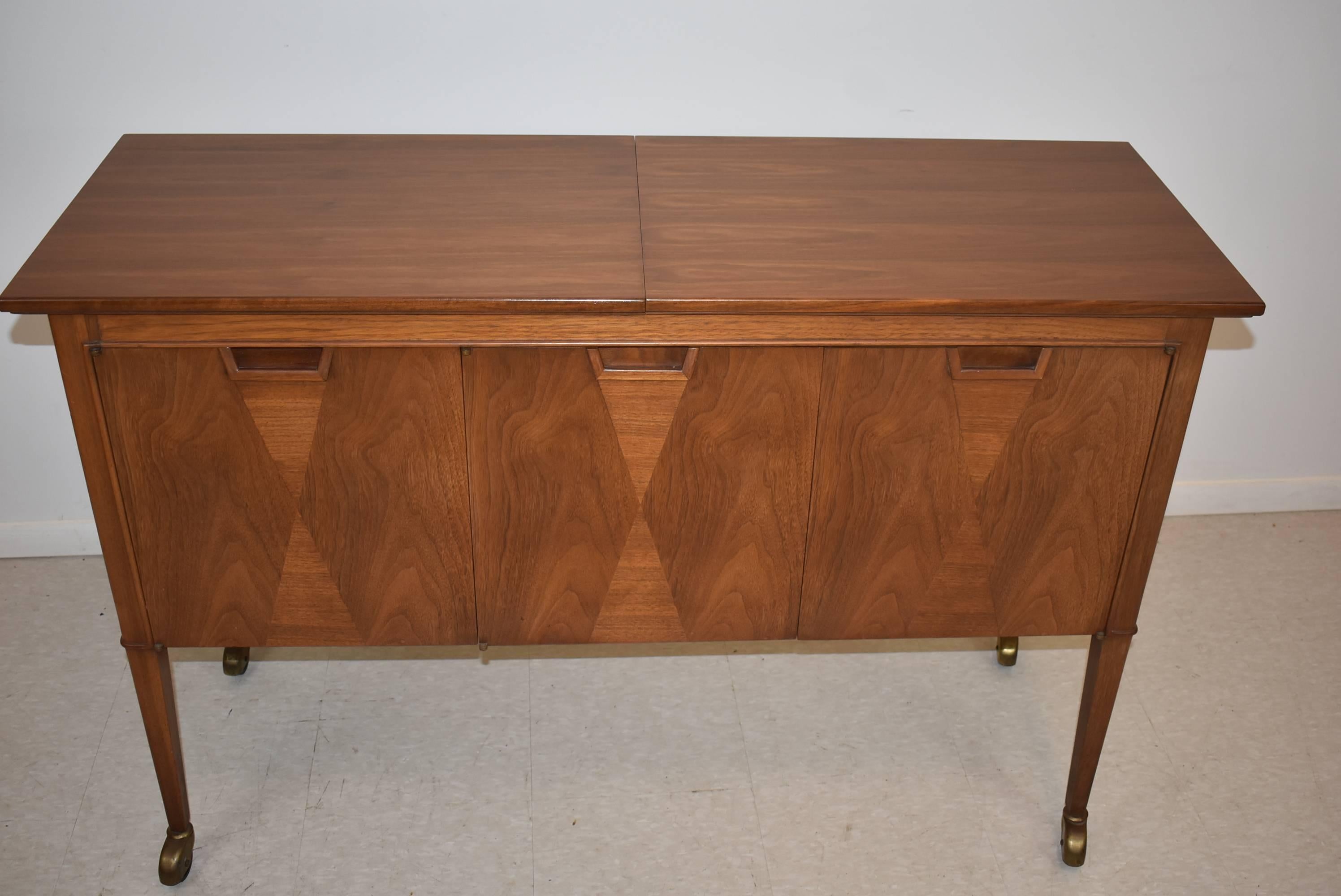 Mid-Century Modern credenza/rolling bar cart made by the Mount Airy Furniture Co. Of North Carolina- Janus Collection. Walnut bar cart with contrasting Triangle walnut inlays on the doors. This Cart can be placed in the middle of a room or in a