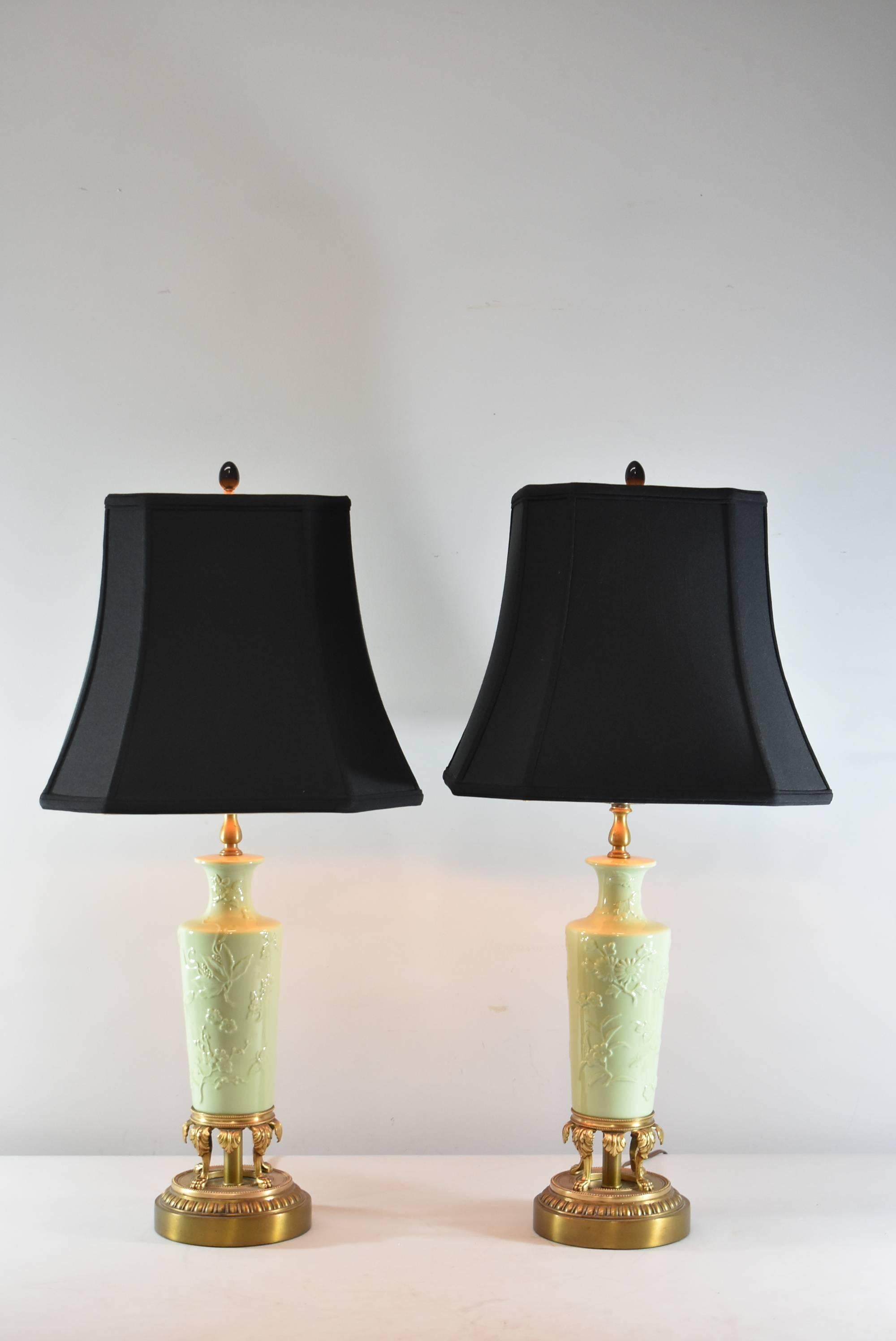 A stunning pair of porcelain table lamps, circa 1930s. They feature a beautiful celadon body with floral details that rests upon a brass base with four claw foot legs. The shades are not included.