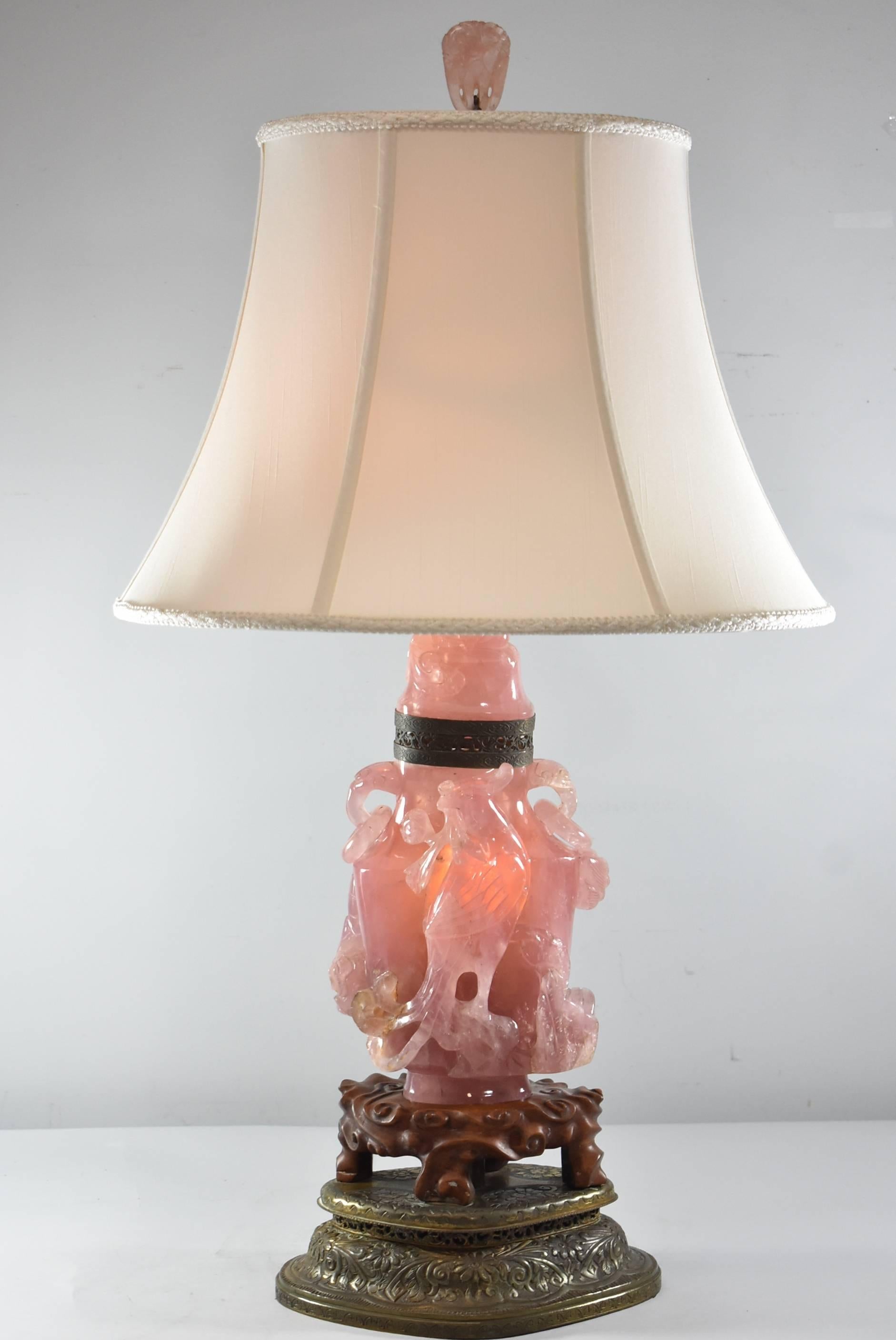 A unique turn of the century Asian rose quartz table lamp. Statue is fixed to a teak wood base which sits atop an embossed, impressed and shaped brass Stand with floral motif. The light is lit by two sockets with pull chains. Wiring is good.