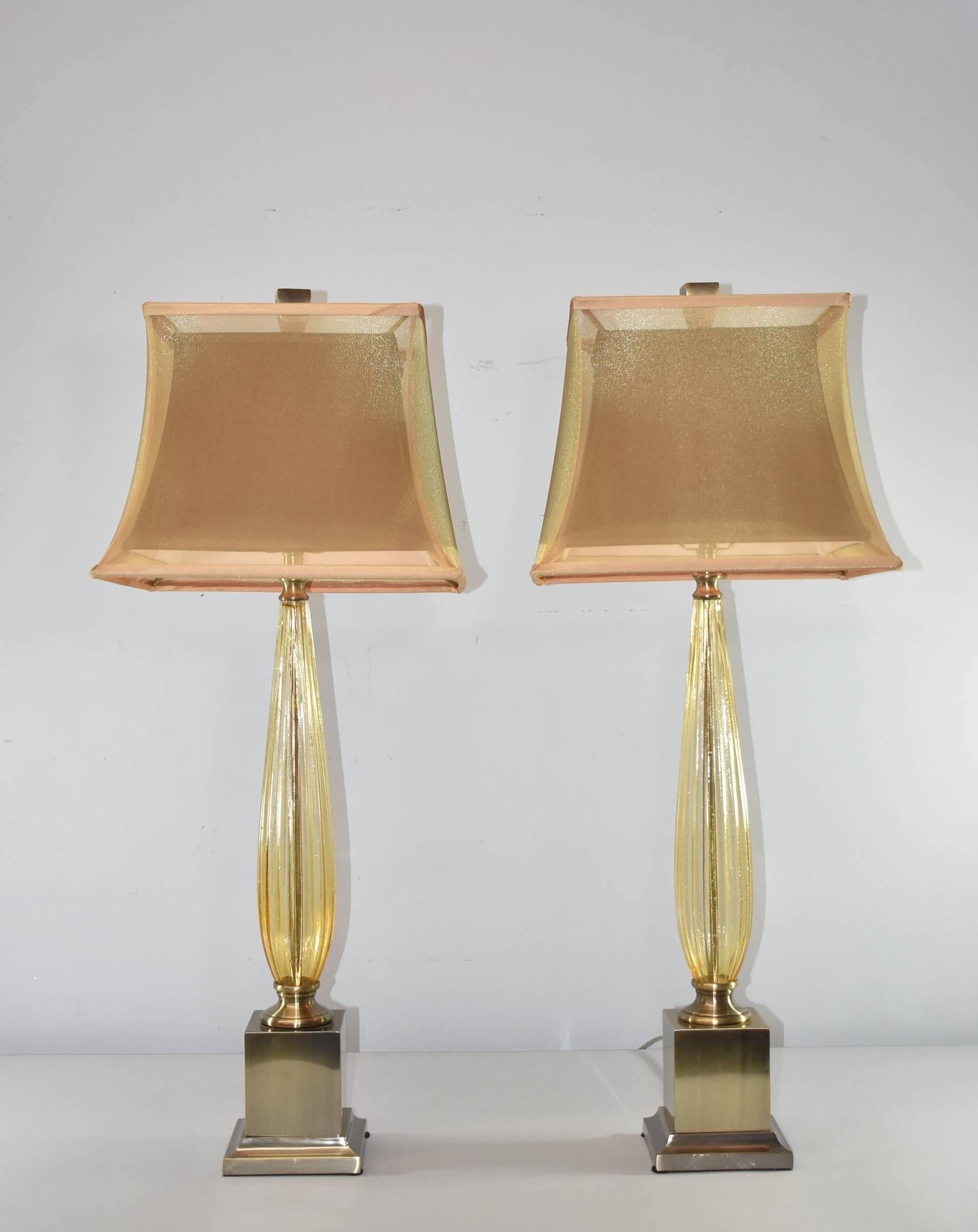 A stunning pair of table lamps by John Richard. Base features antiqued / brushed brass with fluted amber glass. Each lamp is topped with John Richard's signature double shade with translucent silk outer layer. Heavy brass finial finishes the look.