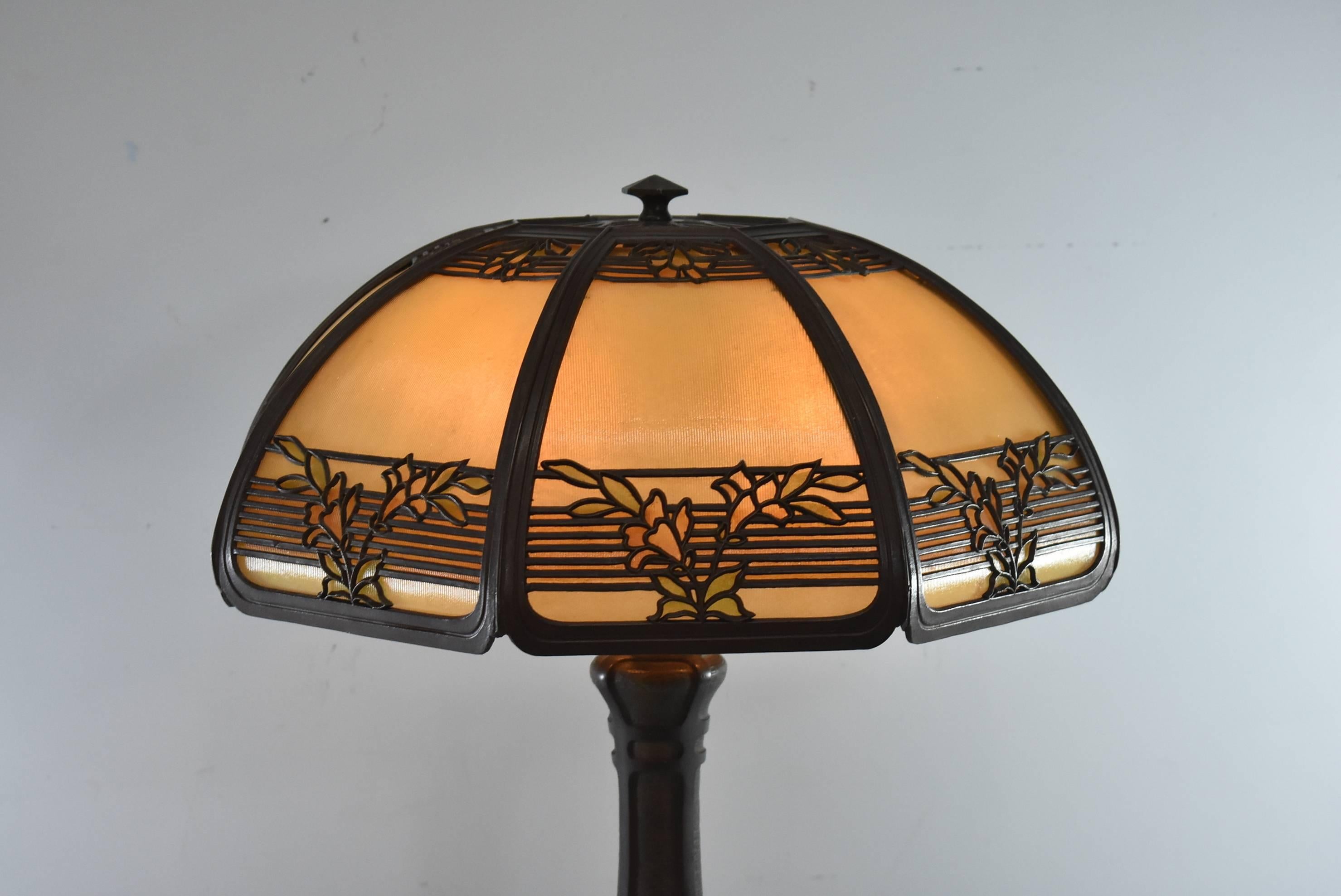 An exceptional bent panel reverse painted glass table lamp by Bradley and Hubbard. The beautiful shade features 8 ribbed panels internally decorated in muted shades of green with a band of light amber and is finished with a gorgeous floral overlay.