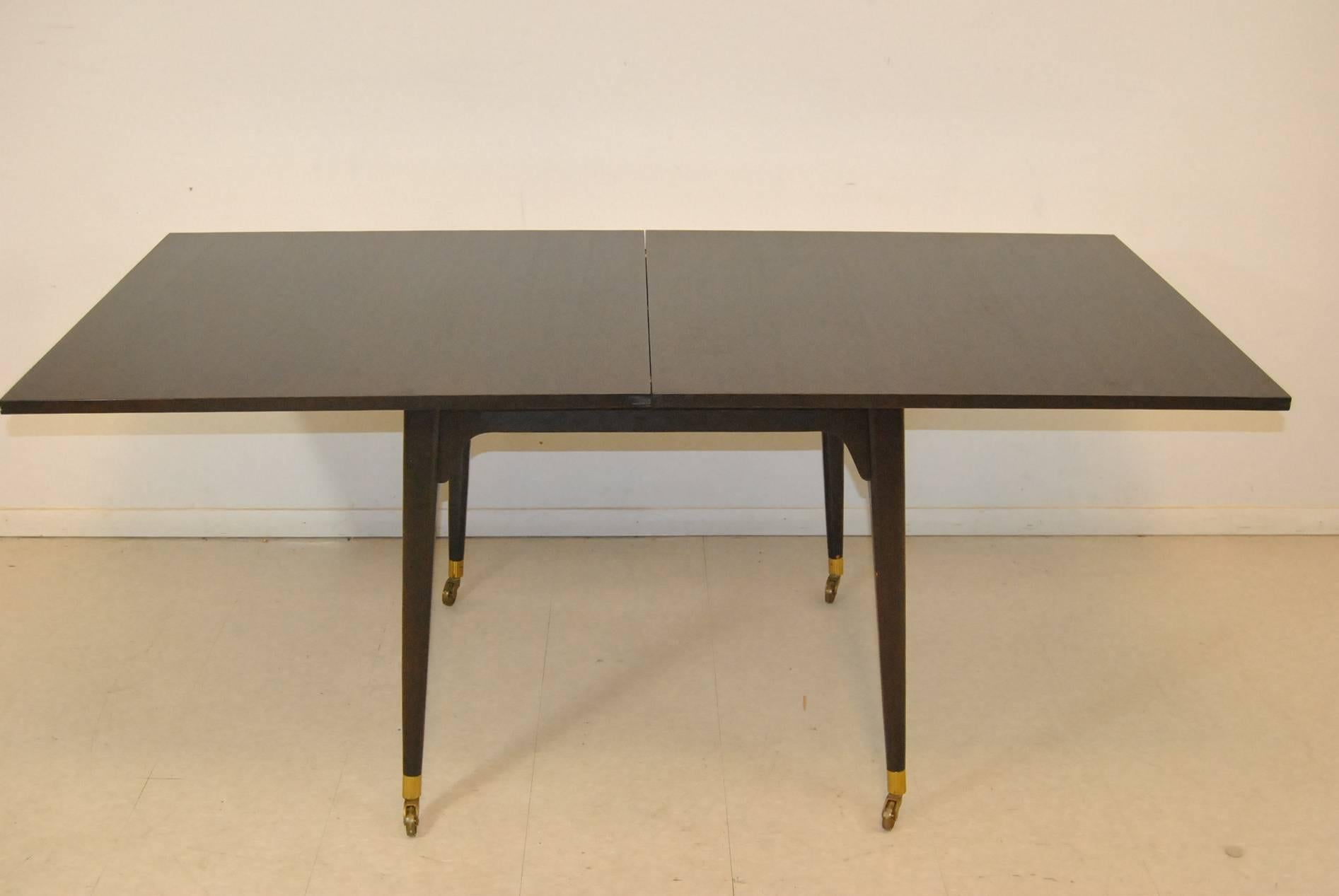 A Mid-Century Modern flip-top game table by Edward Wormley for Dunbar. This fantastic table features heavy brass caster and sleeves, an ebony stain and felt lined storage under the top. The top opens and pivots to make a larger serving surface. Very