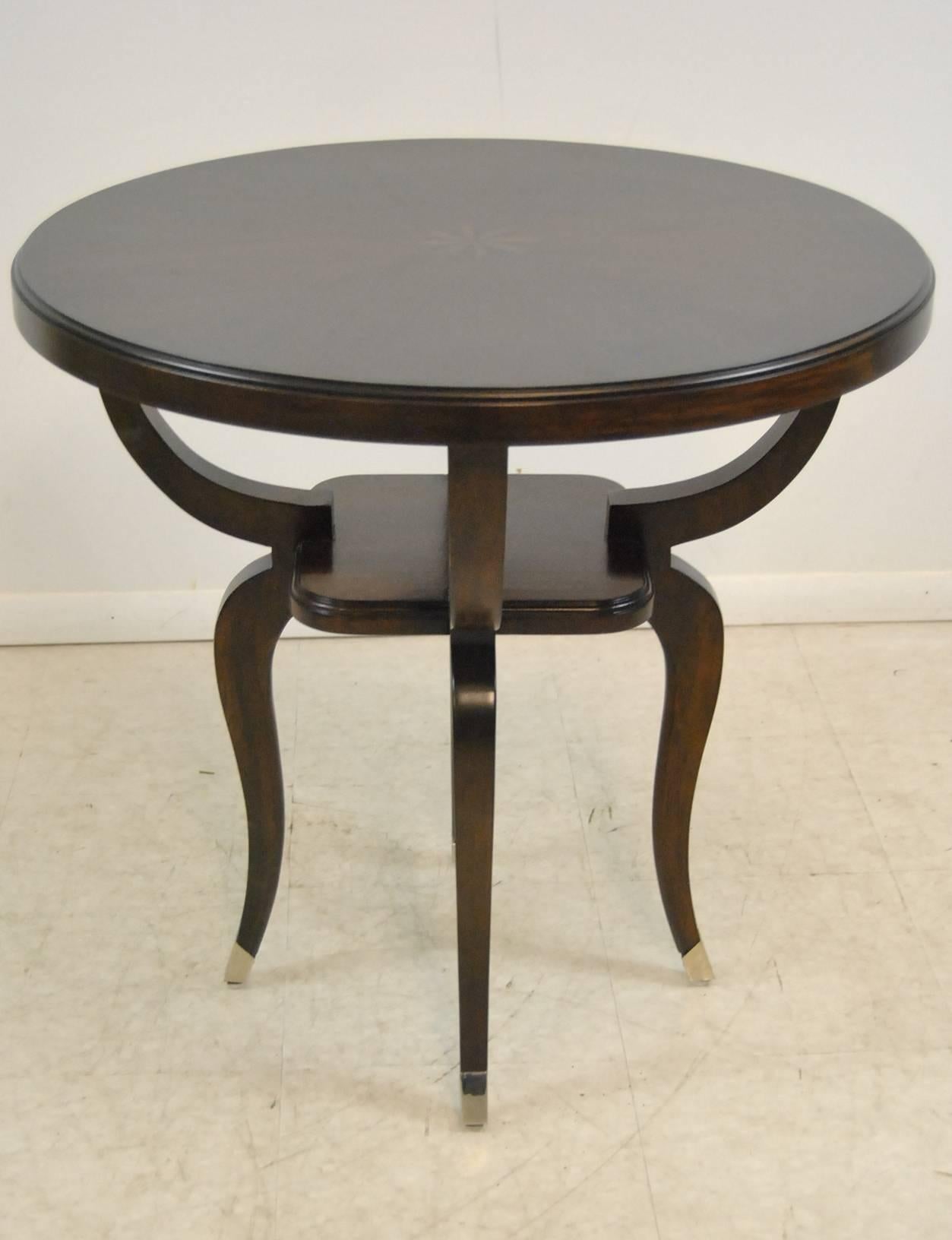 An unusual round end table by Robb & Stucky. The top has an inlaid central medallion. Four curved legs meet in a small central shelf which sits on cabriole legs ending in brass caps. Very good condition, well cared for, ready for use with minimal