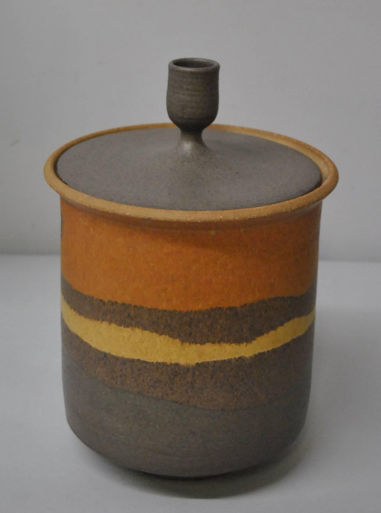 An impressive earthenware vessel with lid by Clydee Burt, 1922-1981.  It features glazed desert shades of gold, terra cotta and browns.  Signed by the artist.  Born in Melrose, OH, Clyde Burt is considered a pioneer is American Art Pottery.  