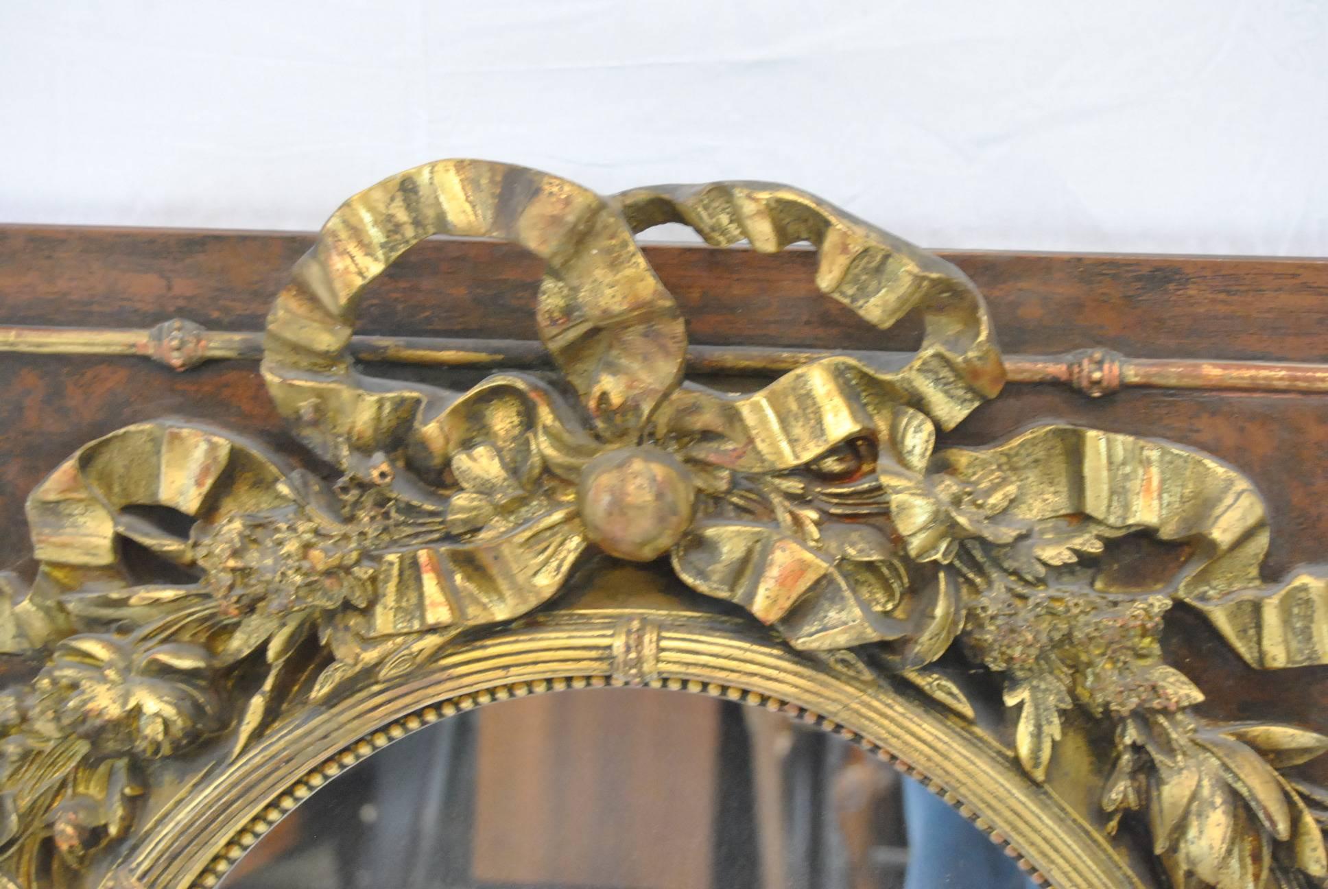 A very unusual Victorian mirror. Mirror is attached to a square frame with brass edge detail. The oval mirror is a golden floral wreath done in high relief with a central bow at top. The mirror is 21