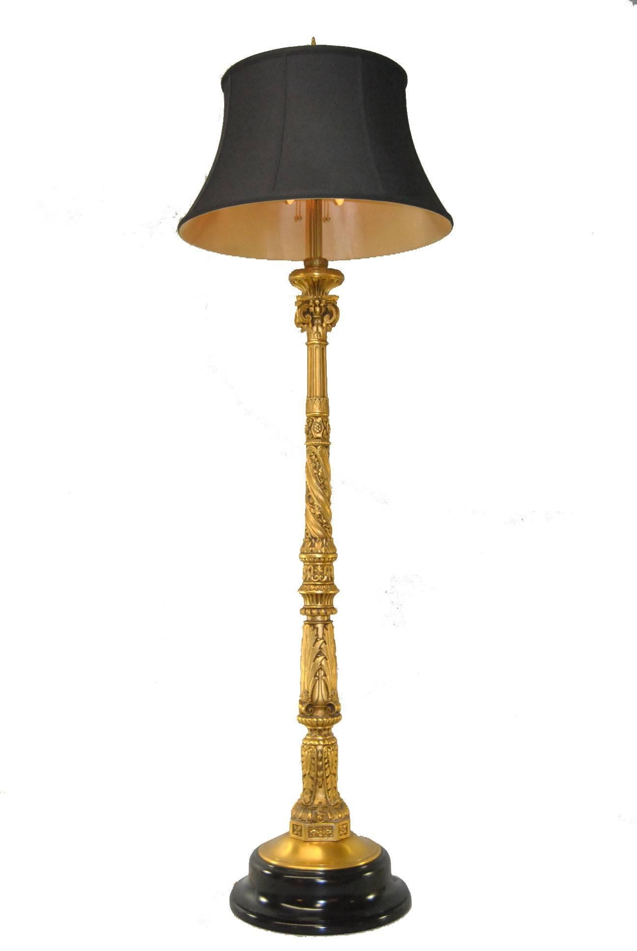 An impressive gilt bronze floor lamp. This turn-of-the-century floor lamp features ornate floral and scroll detailing. Double sockets have brass pulls. The base is black lacquered wood and the lamp has been rewired and is ready for use. The black