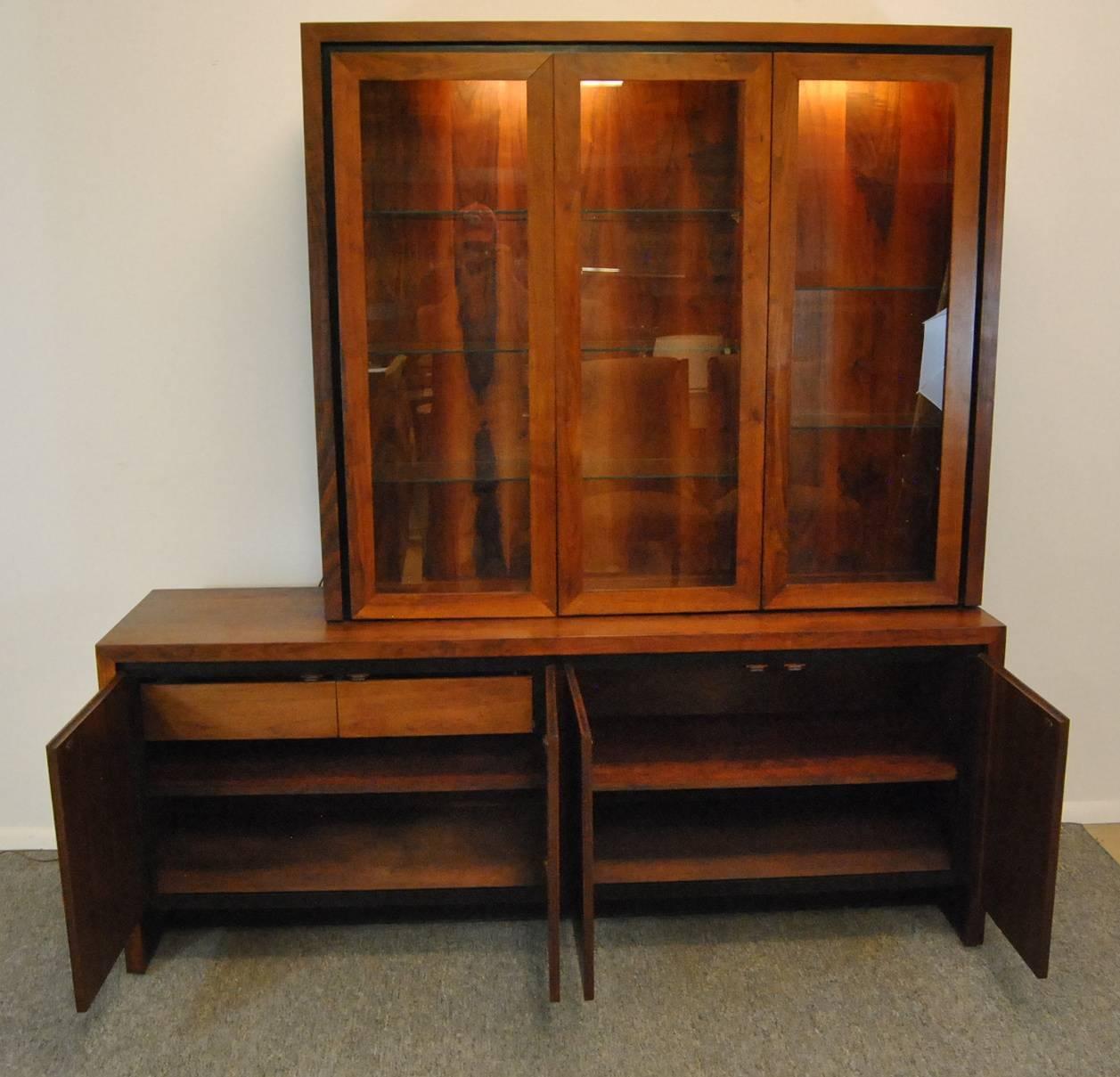 A beautiful Mid-Century Danish modern teak two-piece display cabinet by Dillingham. The top portion of this cabinet has an interior light and three glass doors. The two doors on the left open to three adjustable glass shelves, the door to the right