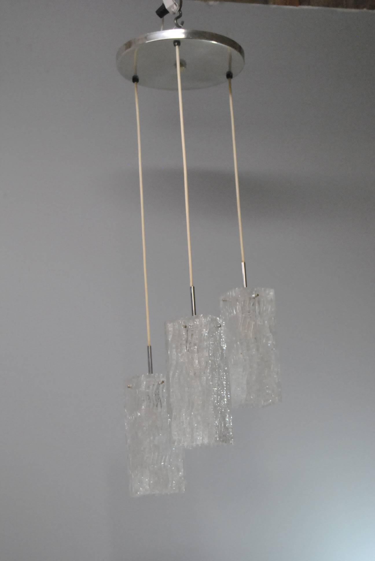 Mid-Century three ice glass pendant chandelier. Attributed to Fagerlund. Glass shades are staggered in length and have a crackled pattern with a wave design running through. The ceiling cap has a silver metal finish. Total length is 37 1/2