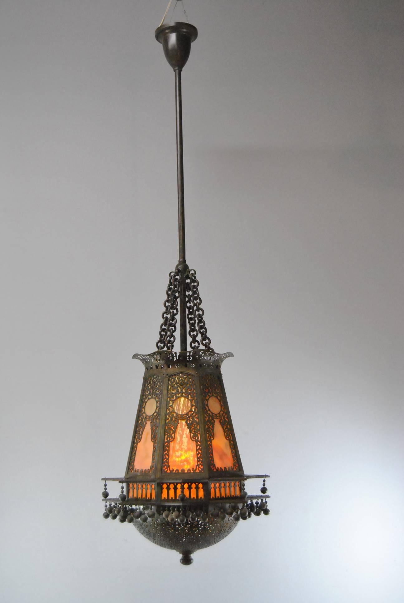 A beautiful Moorish style lantern chandelier by Tiffany Studio. This is eight sided with bronze pierced overlay and stained glass panels. The domed bottom has great open work detailing and opens to a one socket light. Four chains attach to the top