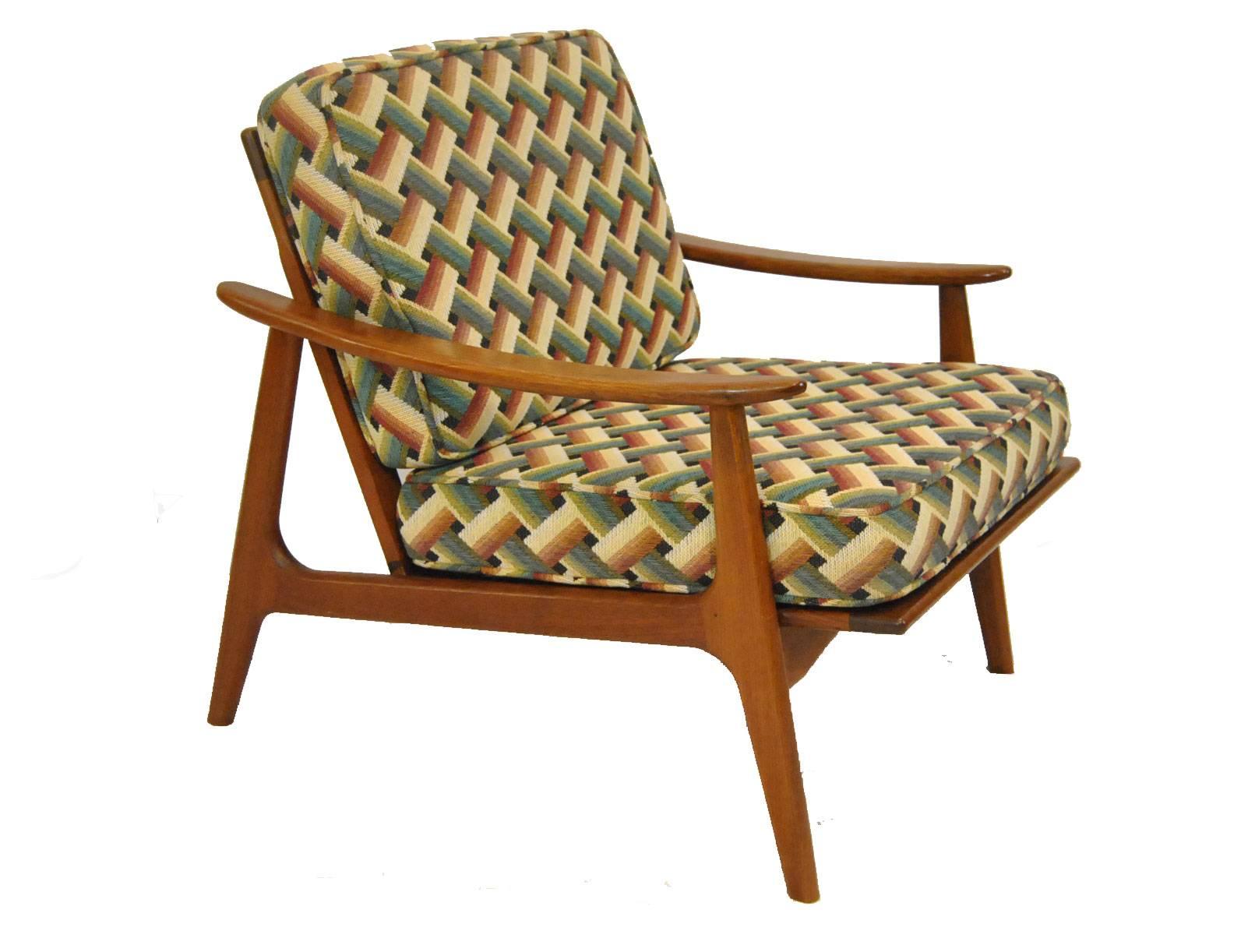 Classic Danish modern lines on this pair of Hans Wegner style teak arm chairs. Chairs feature original cushions with cream, rust and green pattern. Cushions are supported by Fagas straps made by J. M. Birking and Co. frame has clean fluid lines that