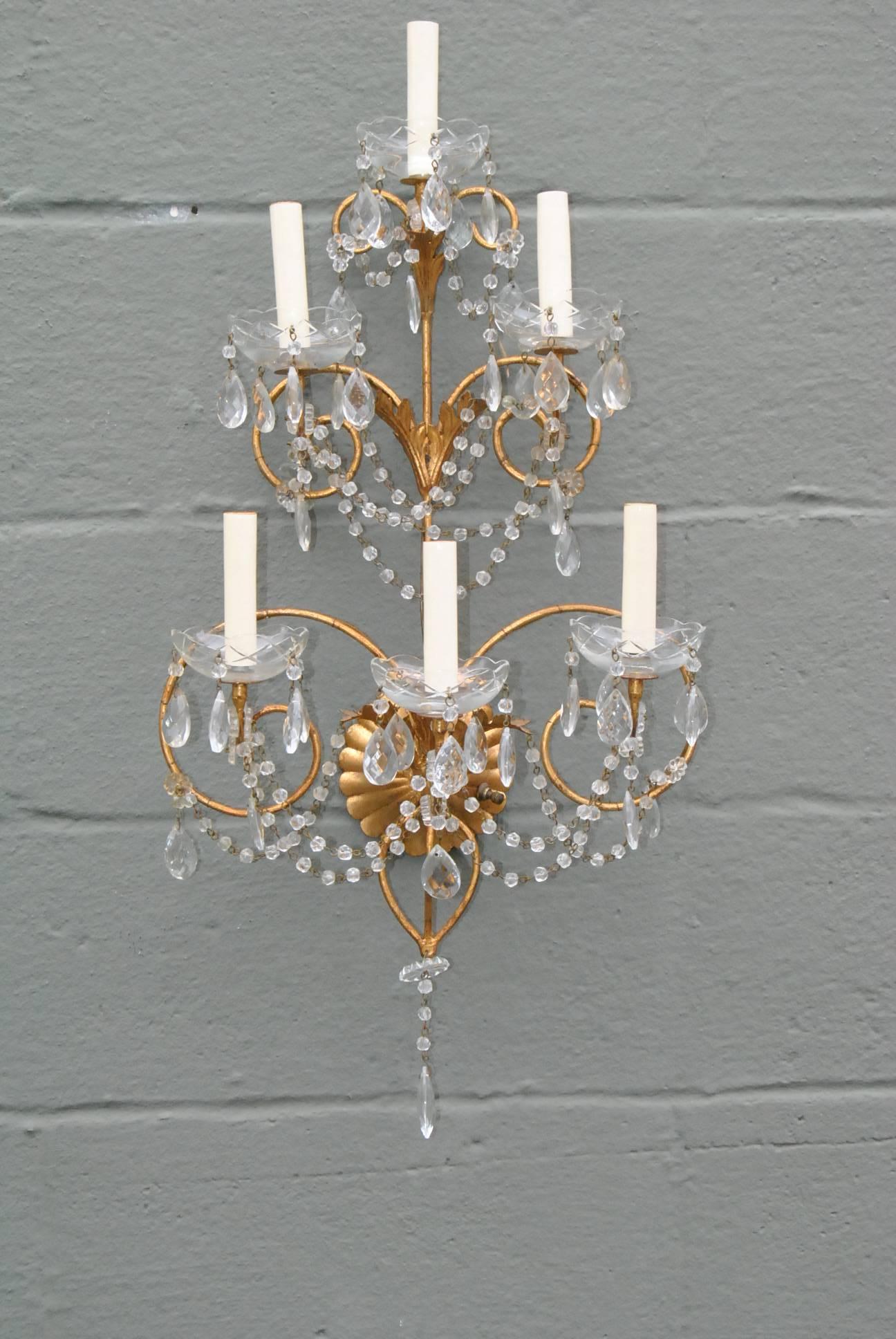 A stunning pair of Italian Maria Theresa Style crystal and gold wall sconces. These ornate pair of sconces feature seven candleabra size sockets that are adorned with beading, draped with swags of crystal strands and have cut crystal bobeches.