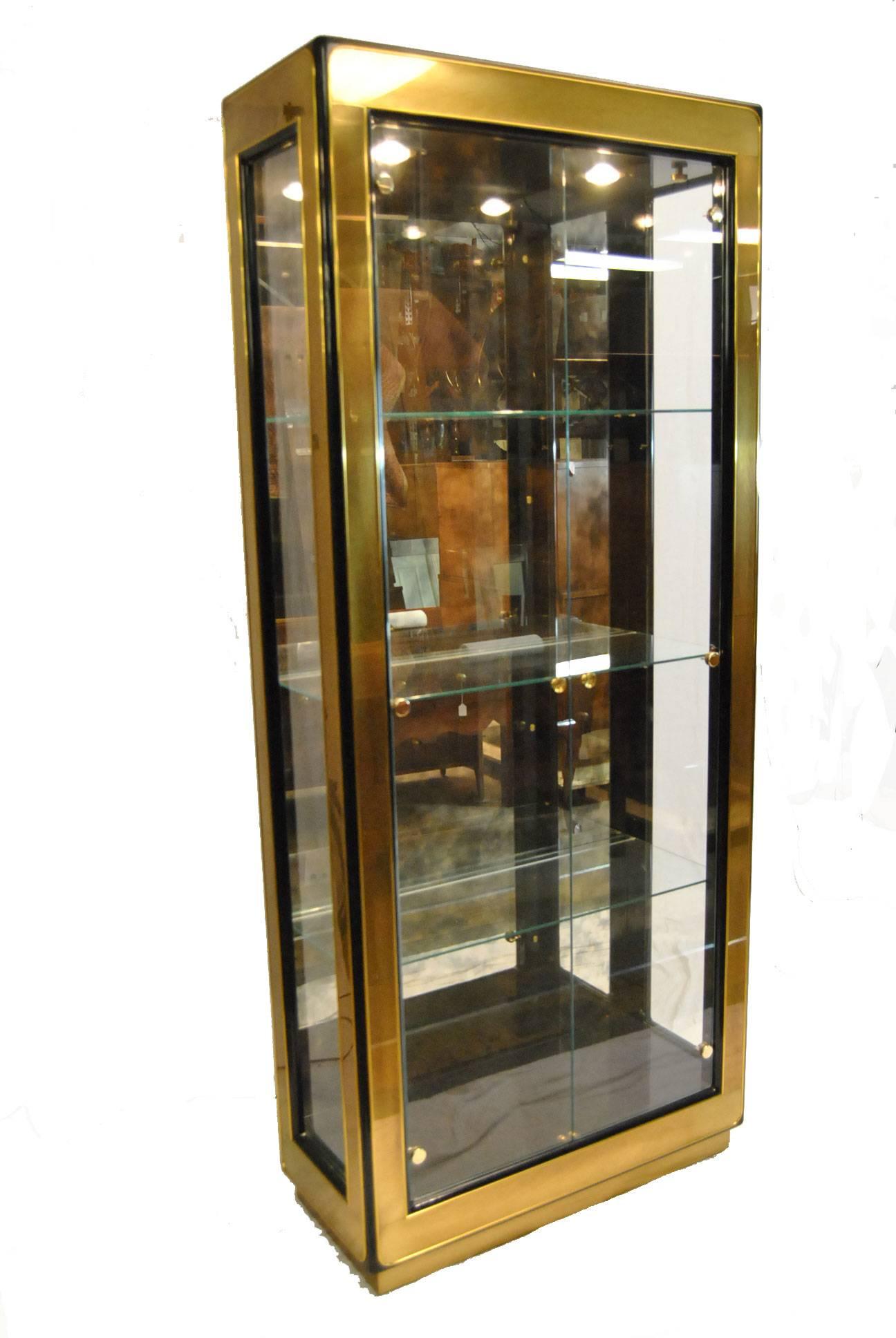 A stunning curio display cabinet by Mastercraft Furniture. This beautiful cabinet features a burnished brass over a black lacquered frame, three adjustable shelves with plate grooves, lights and a distressed smoked mirror on the back interior.