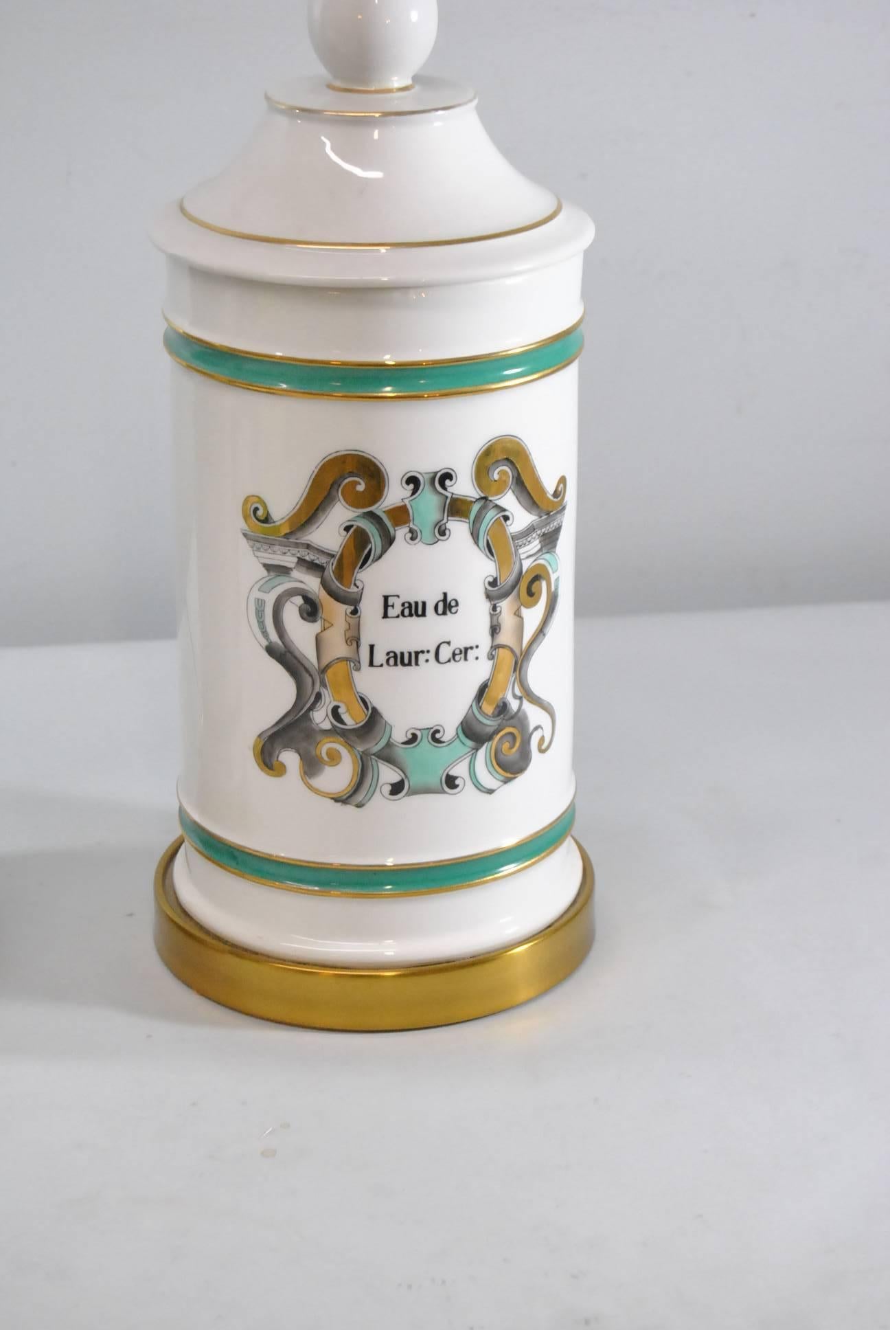 Pair of porcelain table lamps in white with green, black and gold detailing. Classical apothecary jar style with metallic gold trim. Brass openwork at bottom of base. Very good condition, no damage noted. Shades are not included. Base is 32"