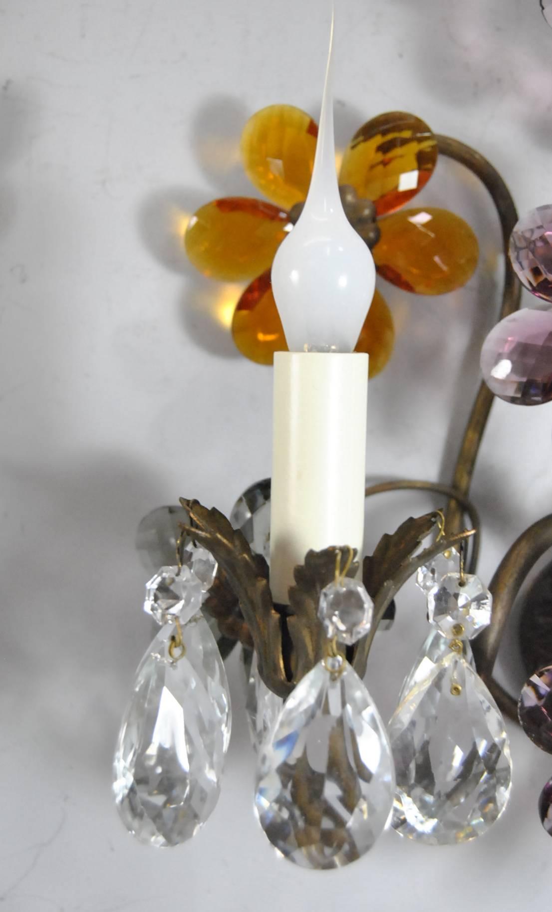 Unique antique pair of French bronze wall sconces. Beautiful floral designs in cut crystal with 12 crystal drops. Glass petals are in shades of amber, lilac and smoke grey. Body has an urn shape which holds two leaf style arms. Measures: 12"