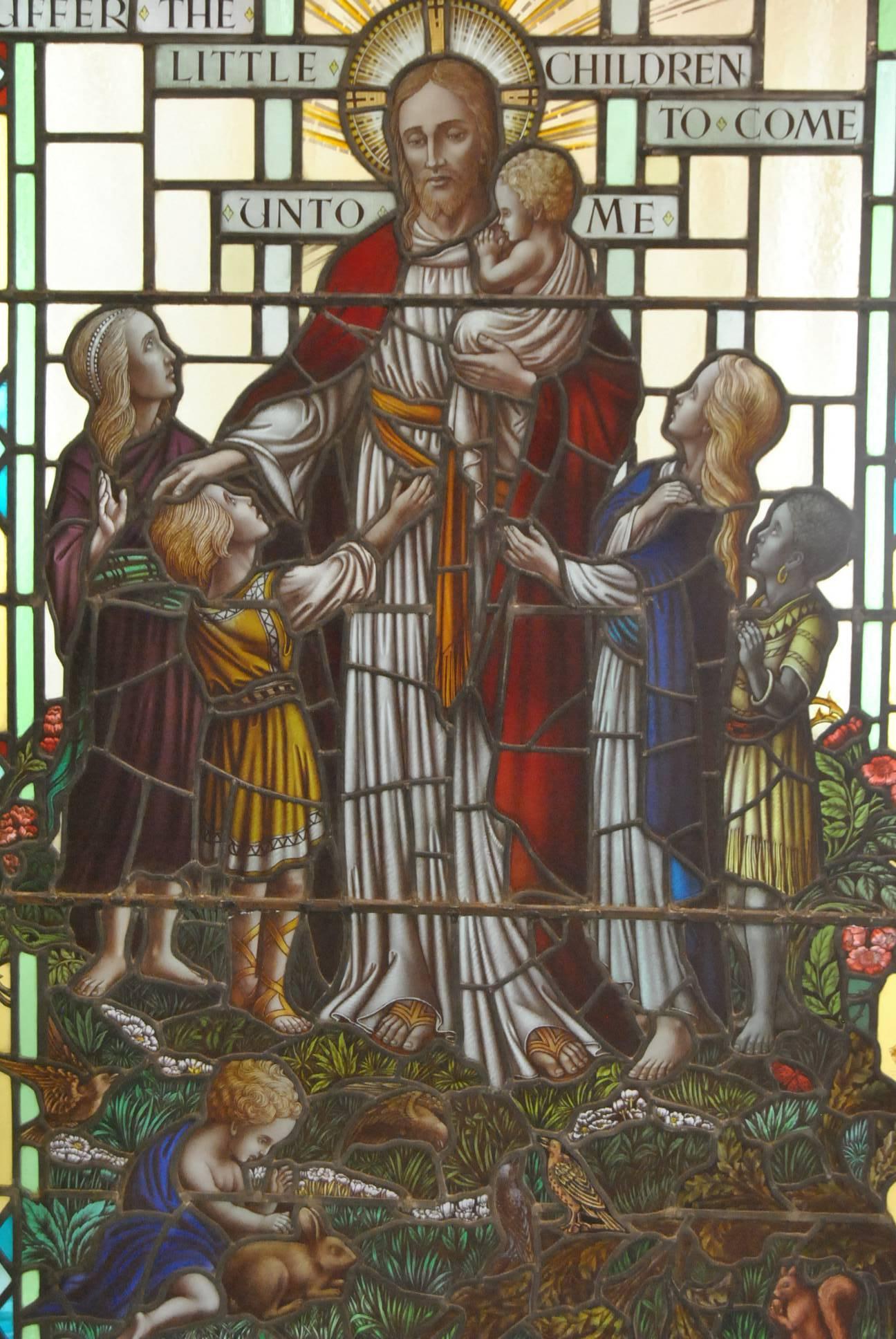 A stunning stained glass window from an American church. It depicts Jesus surrounded by children. It reads, "Suffer, Let the Children Come Unto Me" and the lower right "To the Glory of God" with a dedication. Brilliant colors