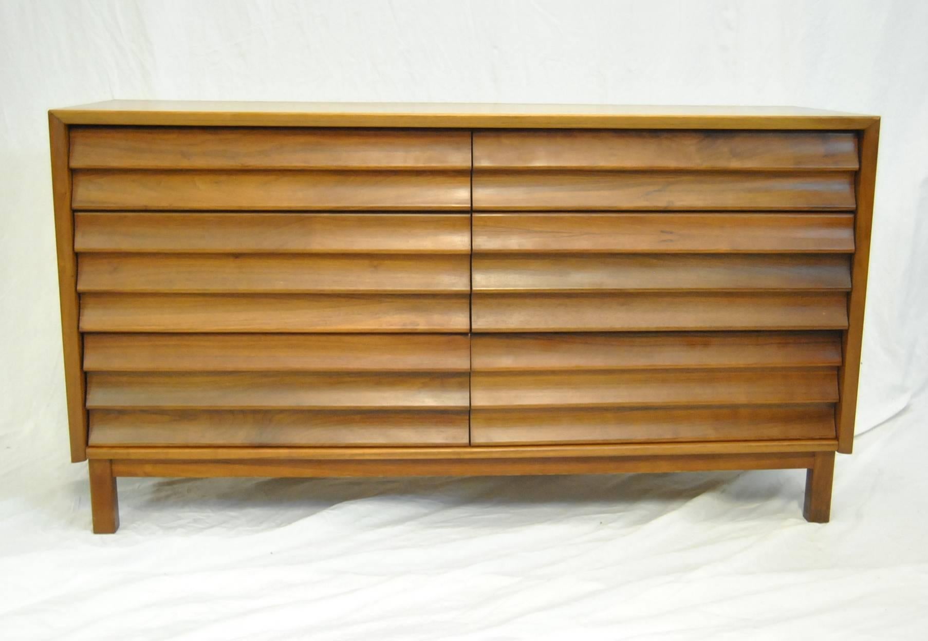 A pair of louvered front walnut dressers by American Martinsville. Each dresser has six drawers. The dressers are done in Wonder Wood which is a layer of walnut veneer layered with vinyl and heat dispersing foil which allows the finish to resist