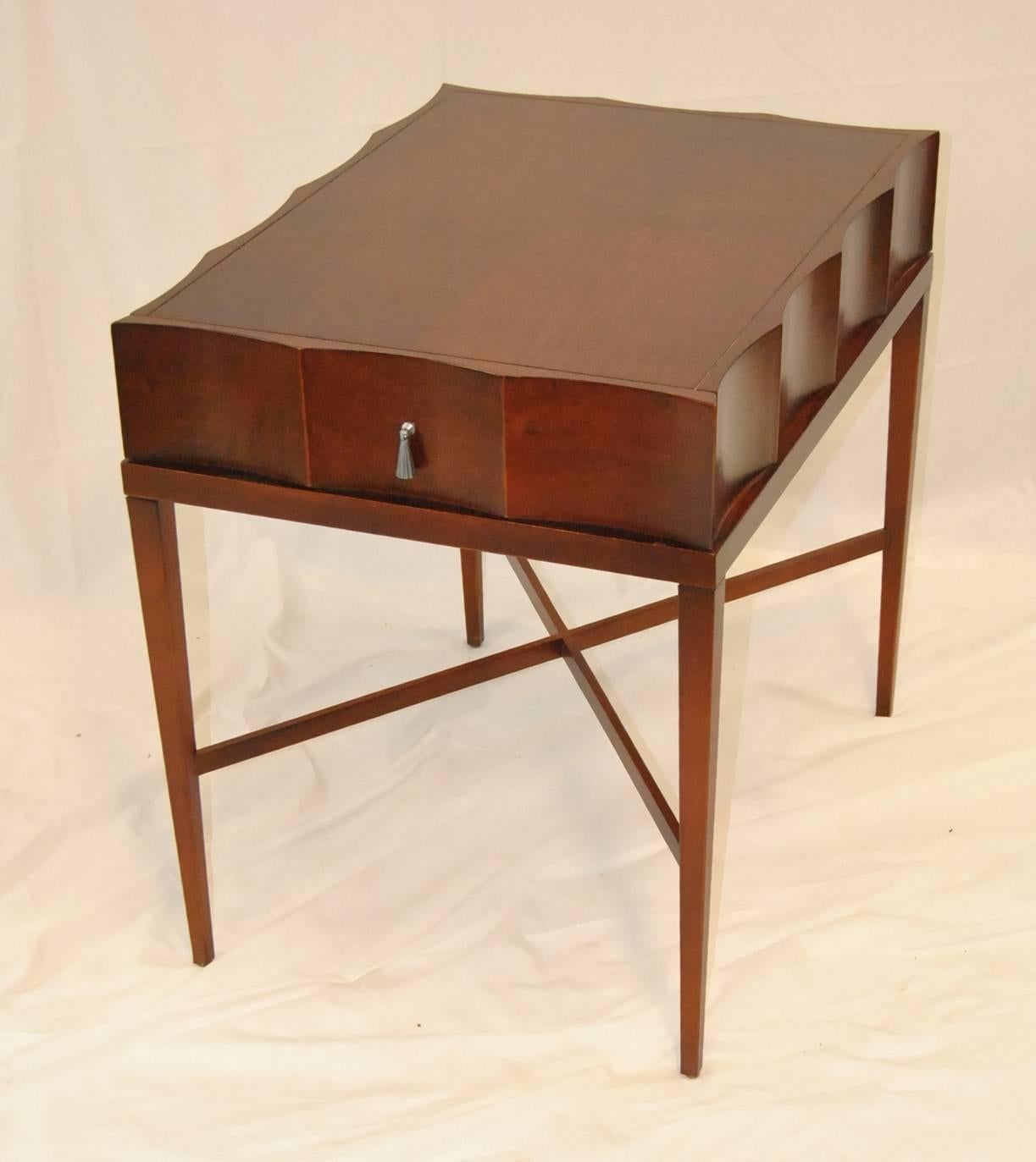 A unique mahogany side table by Baker Furniture. The small-scale table is big on style. The top is scalloped and features a front drawer with pewter pull. Top sits on four tapered legs with stretchers which not only provide a design feature but add