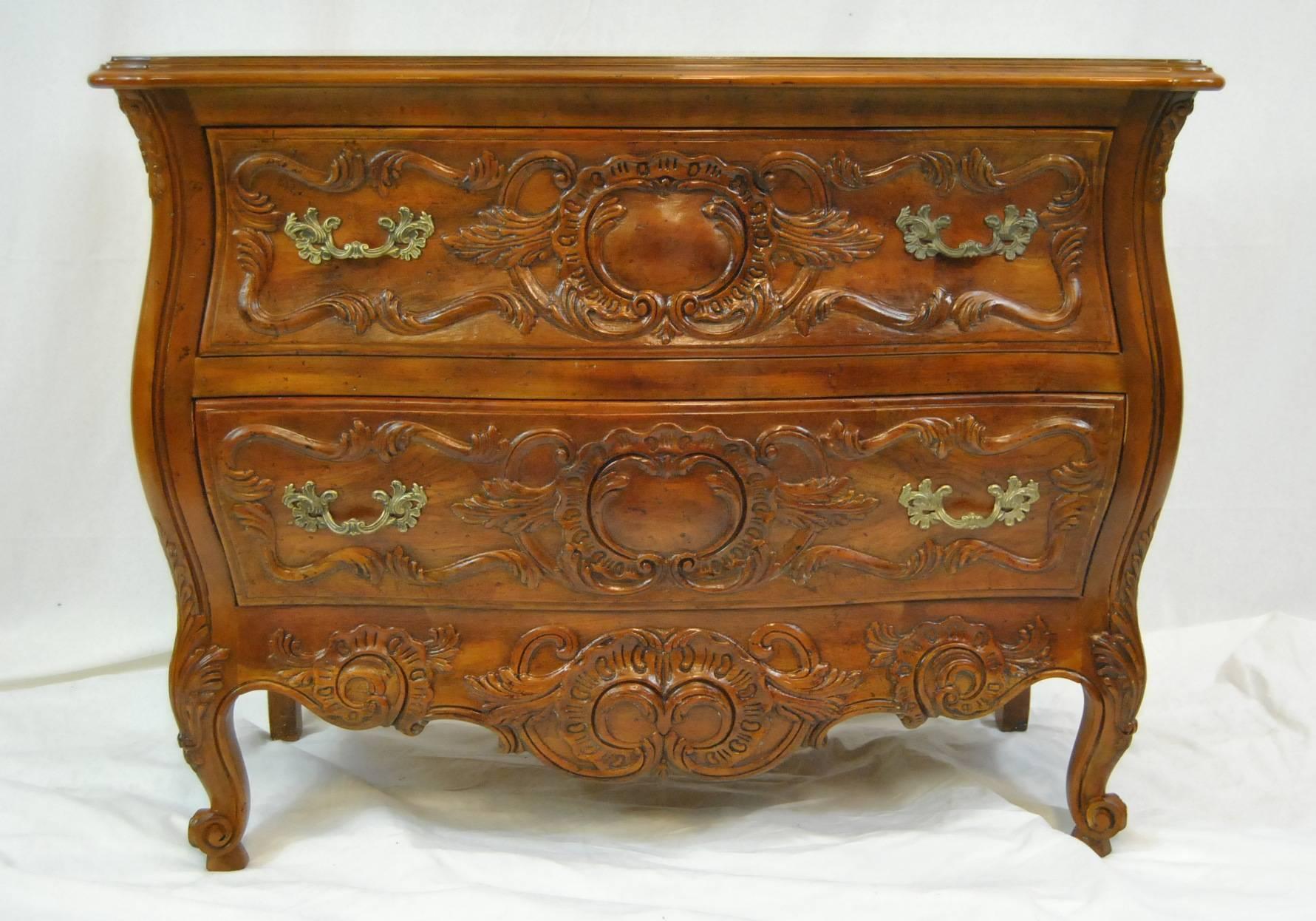 A beautiful walnut two-drawer bombe chest by John Widdicomb carved walnut chests drawer fronts are accented with scrolling foliage motifs.. The chest is raised on four legs, the front two cabriole legs terminating in scrolled feet. Hardware is