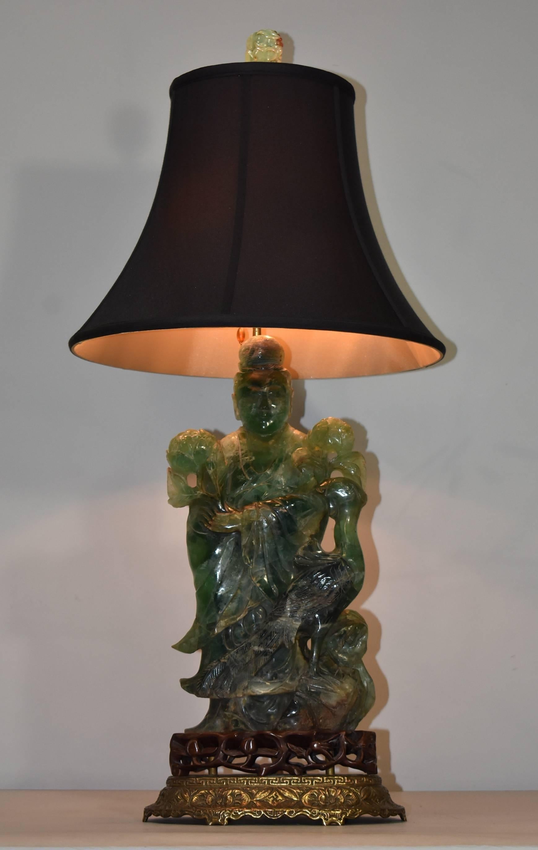 A unique large-scale turn of the century lamp. The lamp features a green quartz carved statue of Quan Yin with her peacock. Statue is afixed to a pierced teakwood base which sits atop an embossed, impressed and shaped Brass Stand with floral motif.