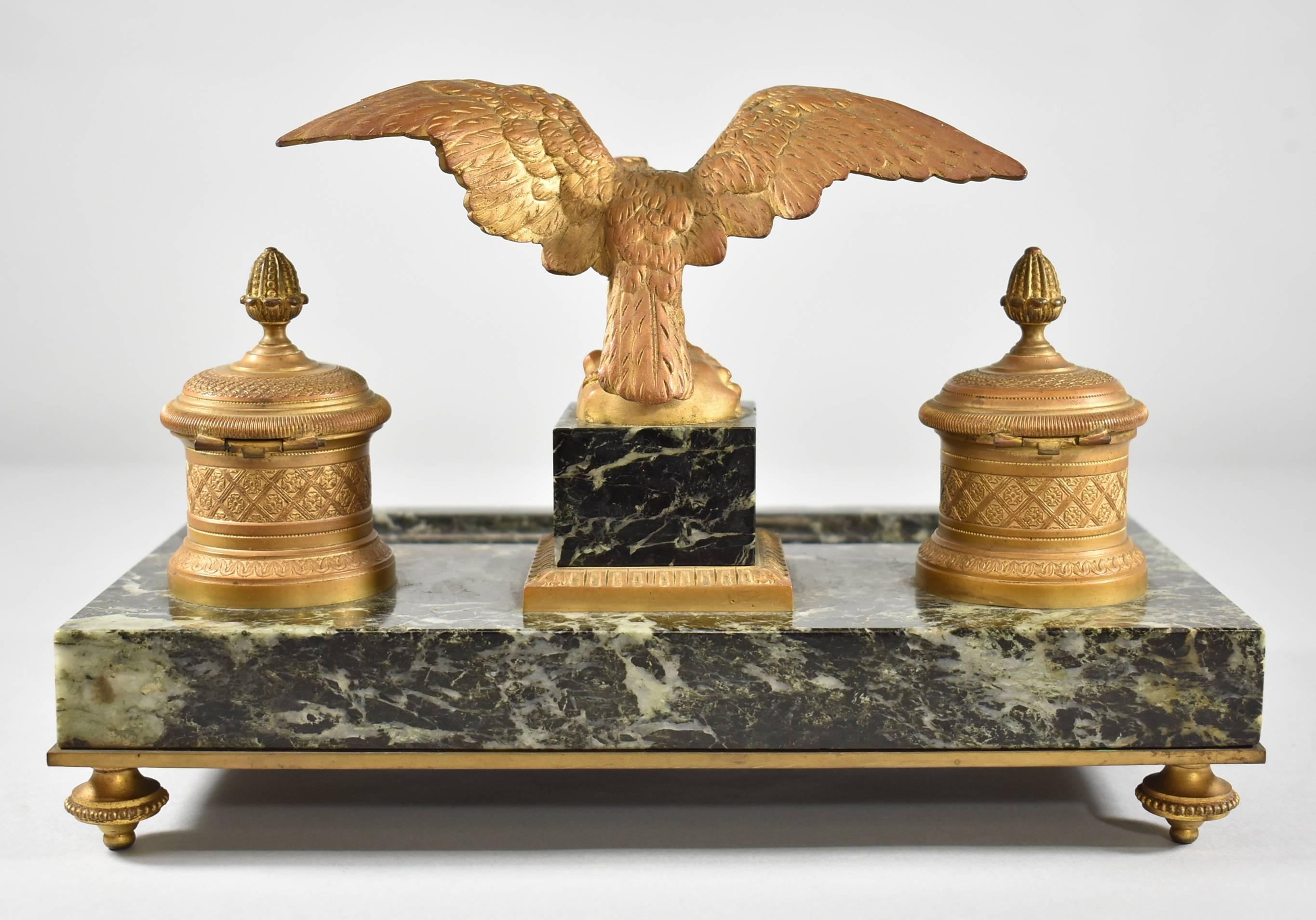 A large 19th century French gilt bronze and marble inkwell. Featured are an eagle perched atop a central plinth with outspread wings flanked by two bronze covered inkwells with glass inserts. Bronze mounts adorn the plinth and the front of the