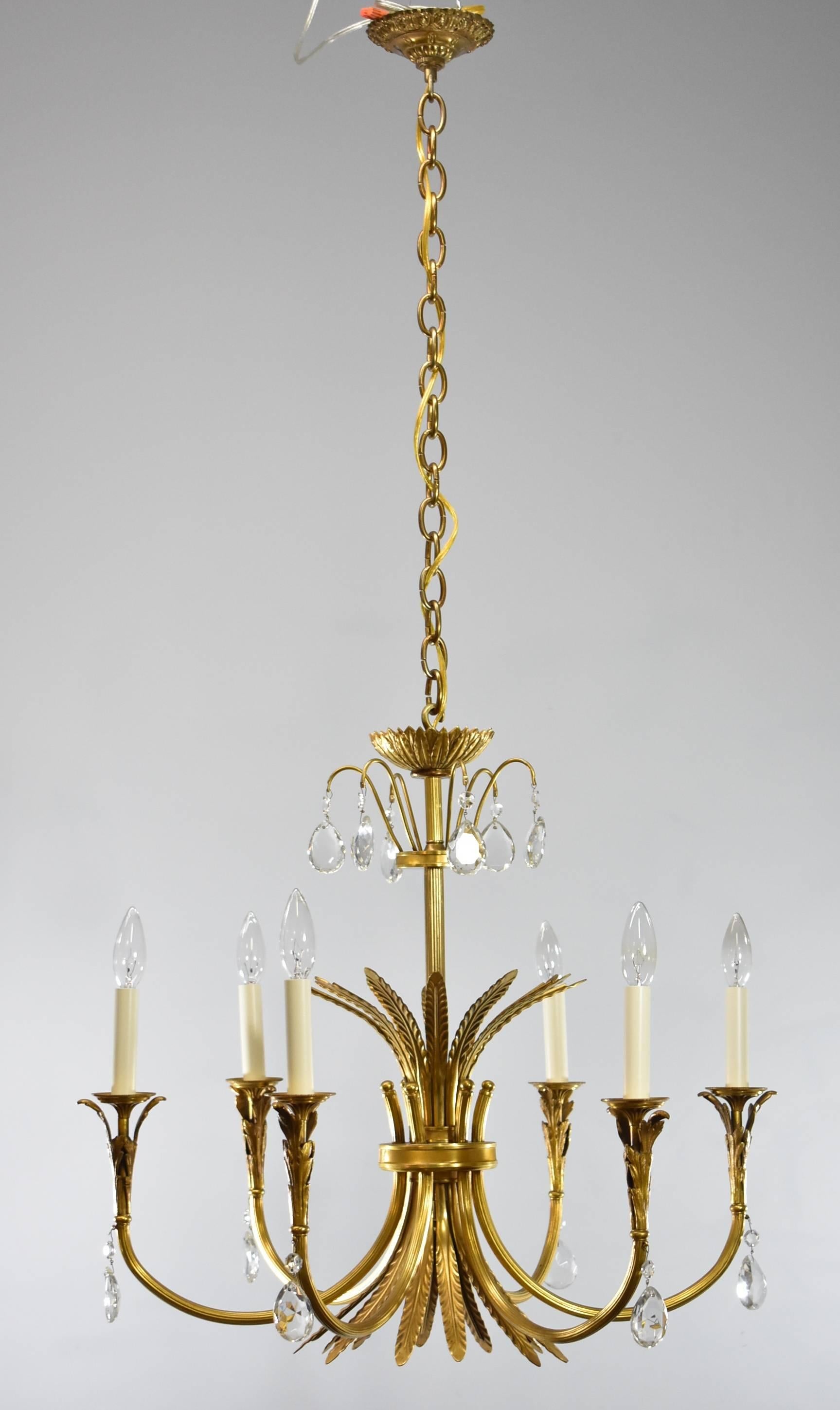 A beautiful Italian Neoclassic style six-arm brass chandelier with crystal accents. The central sheaf design body has six arms with leaf detailing at brass bobeche holding white candlesticks. At the top is a crown of featuring six crystal drop